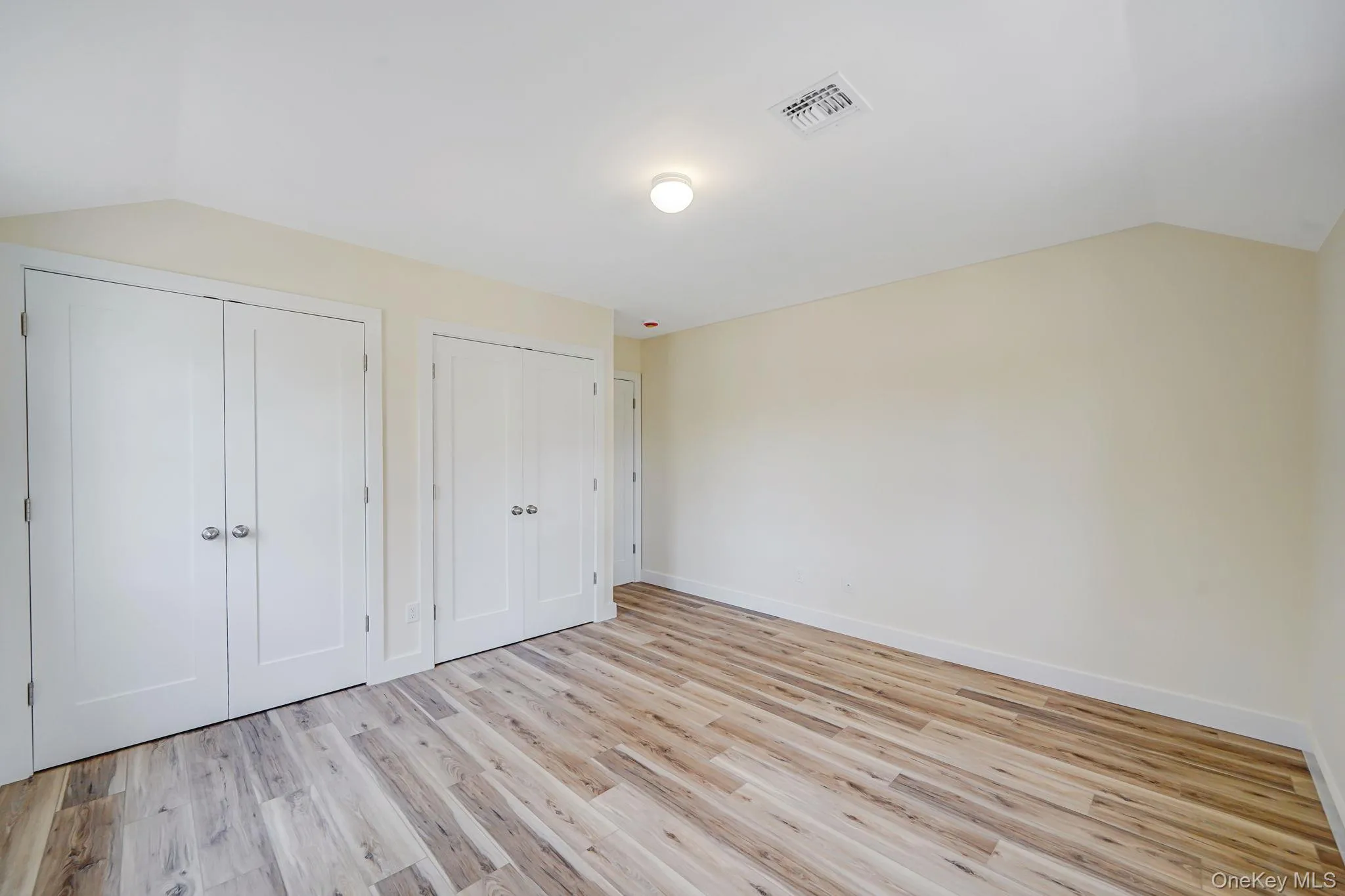 Unfurnished bedroom with multiple closets, vaulted ceiling, light wood-style flooring, and baseboards Unfurnished bedroom with multiple closets, vaulted ceiling, light wood-style flooring, and baseboards