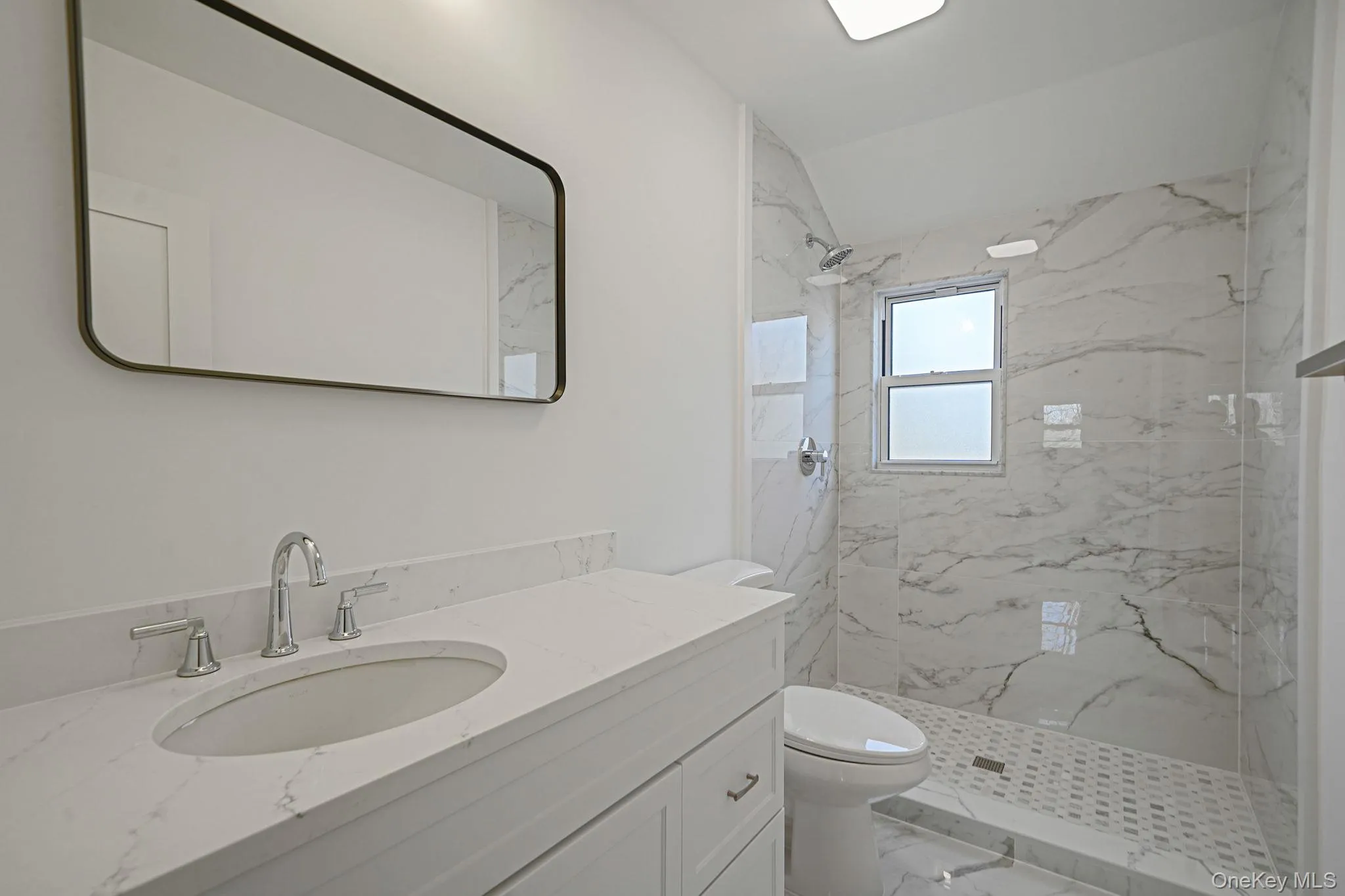 Full bath with marble look tile flooring, toilet, vanity, and a marble finish shower Full bath with marble look tile flooring, toilet, vanity, and a marble finish shower