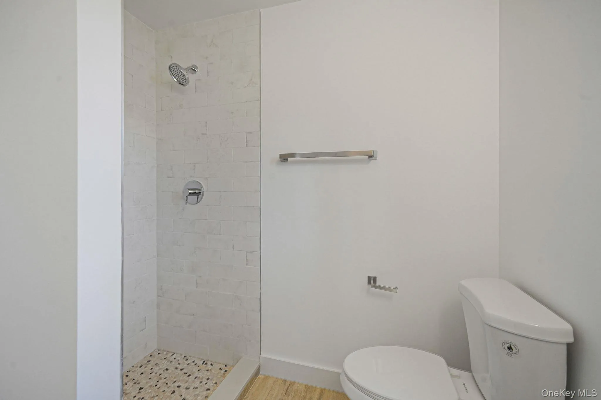 Bathroom with toilet, a tile shower, and wood finished floors Bathroom with toilet, a tile shower, and wood finished floors