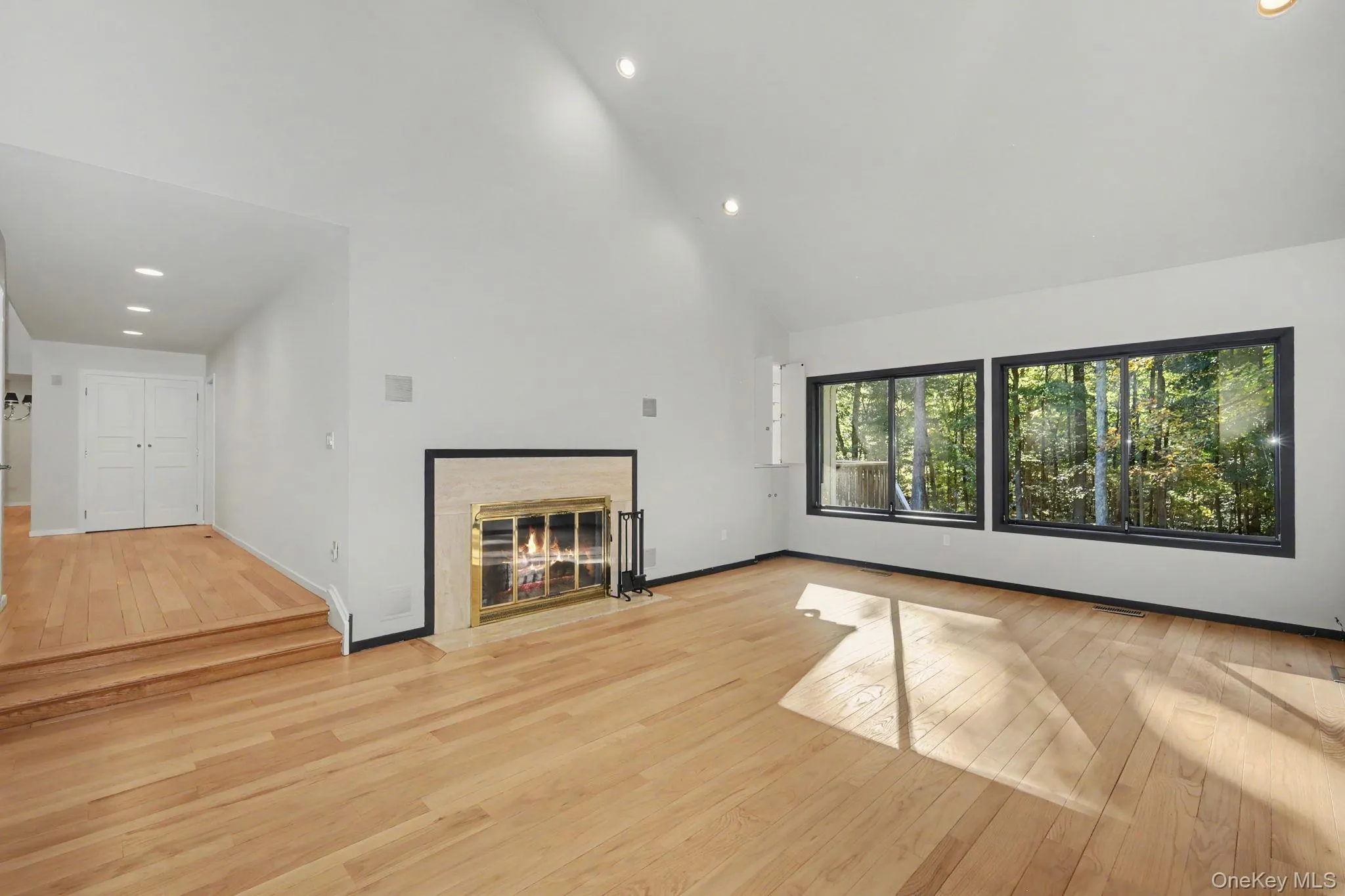 Generous living room with cathedral ceilings, fireplace, and expansive windows overlooking the wooded grounds. Generous living room with cathedral ceilings, fireplace, and expansive windows overlooking the wooded grounds.