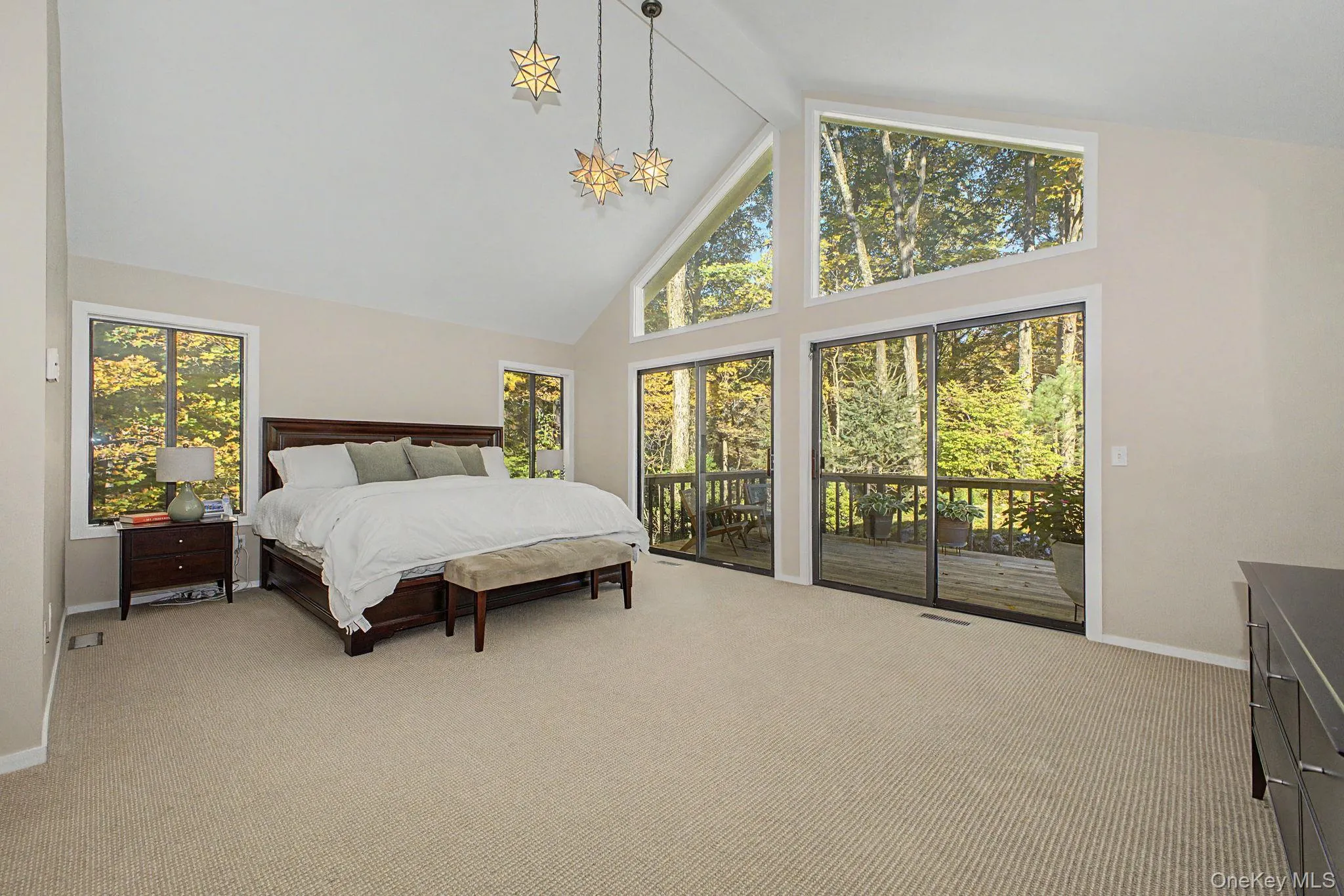 Primary bedroom retreat with soaring cathedral ceilings, expansive windows, and sliding doors to a private deck overlooking the wooded grounds. Primary bedroom retreat with soaring cathedral ceilings, expansive windows, and sliding doors to a private deck overlooking the wooded grounds.