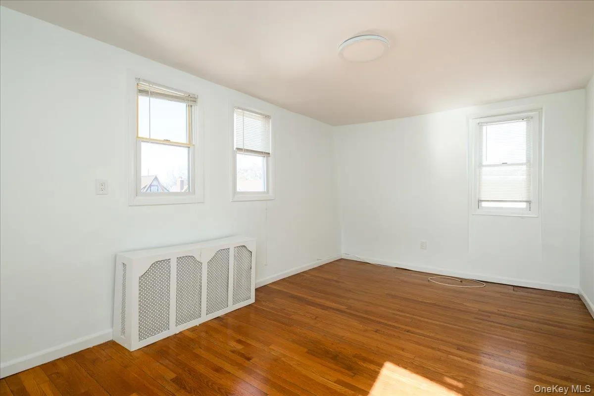 Second Floor Bedroom featuring wood-finish flooring, three double-hung windows, and a decorative built-in radiator cover with latticework detailing Second Floor Bedroom featuring wood-finish flooring, three double-hung windows, and a decorative built-in radiator cover with latticework detailing