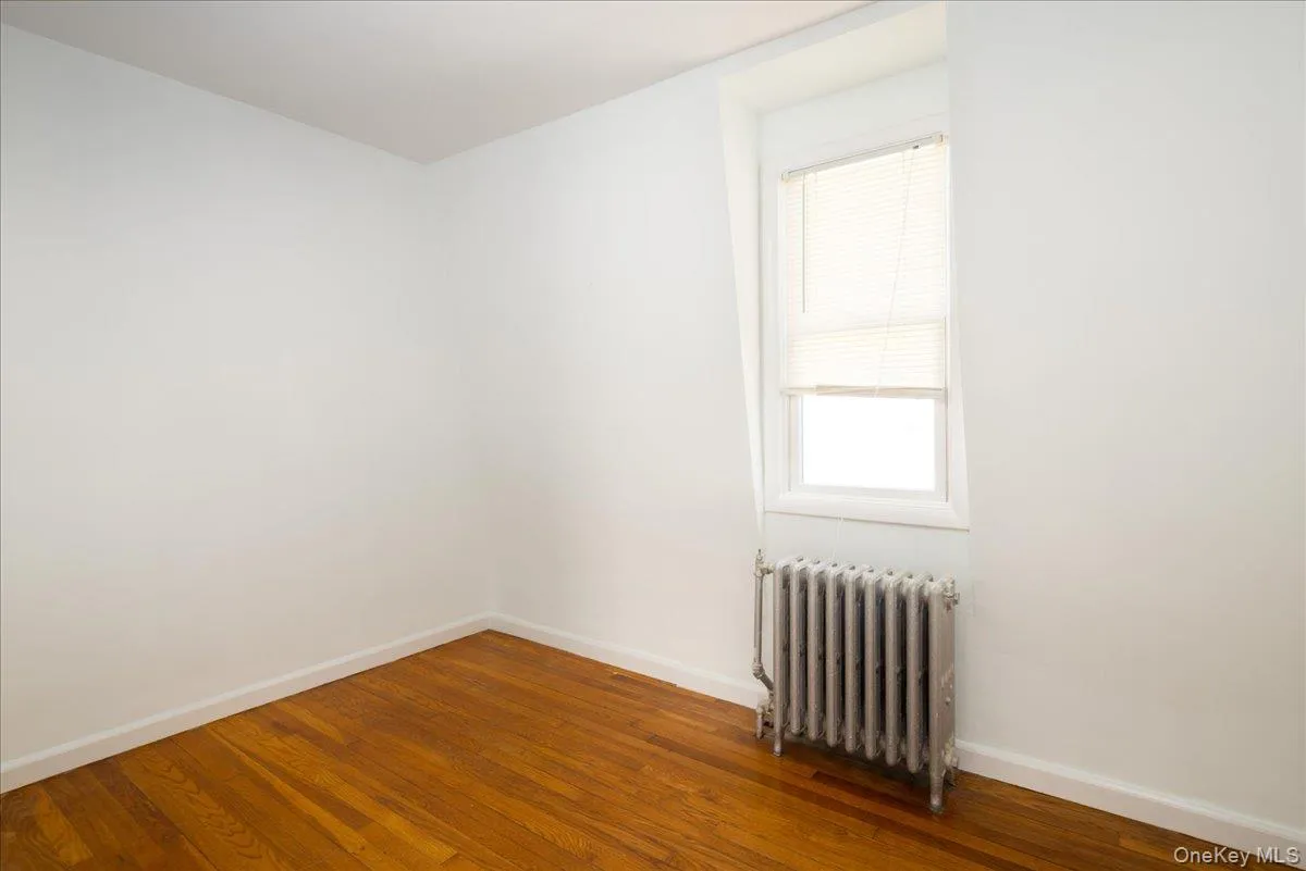 Second Floor. Bedroom #2 featuring wood-finish flooring, a single-pane window with integrated blinds, and a cast-iron radiator Second Floor. Bedroom #2 featuring wood-finish flooring, a single-pane window with integrated blinds, and a cast-iron radiator
