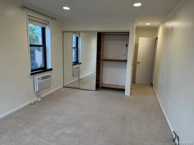 Window with black trim, built-in shelving, mirrored closet doors, recessed lighting, and light-toned carpeting Window with black trim, built-in shelving, mirrored closet doors, recessed lighting, and light-toned carpeting