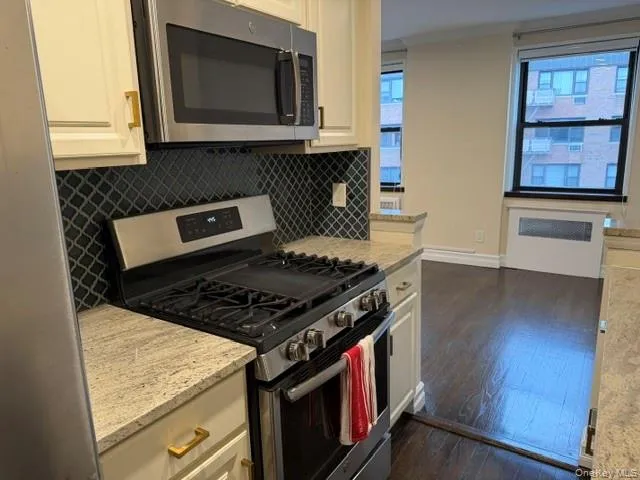 Stainless steel range with an overhead microwave, stone countertops, trellis-patterned backsplash, and wood-finish flooring Stainless steel range with an overhead microwave, stone countertops, trellis-patterned backsplash, and wood-finish flooring