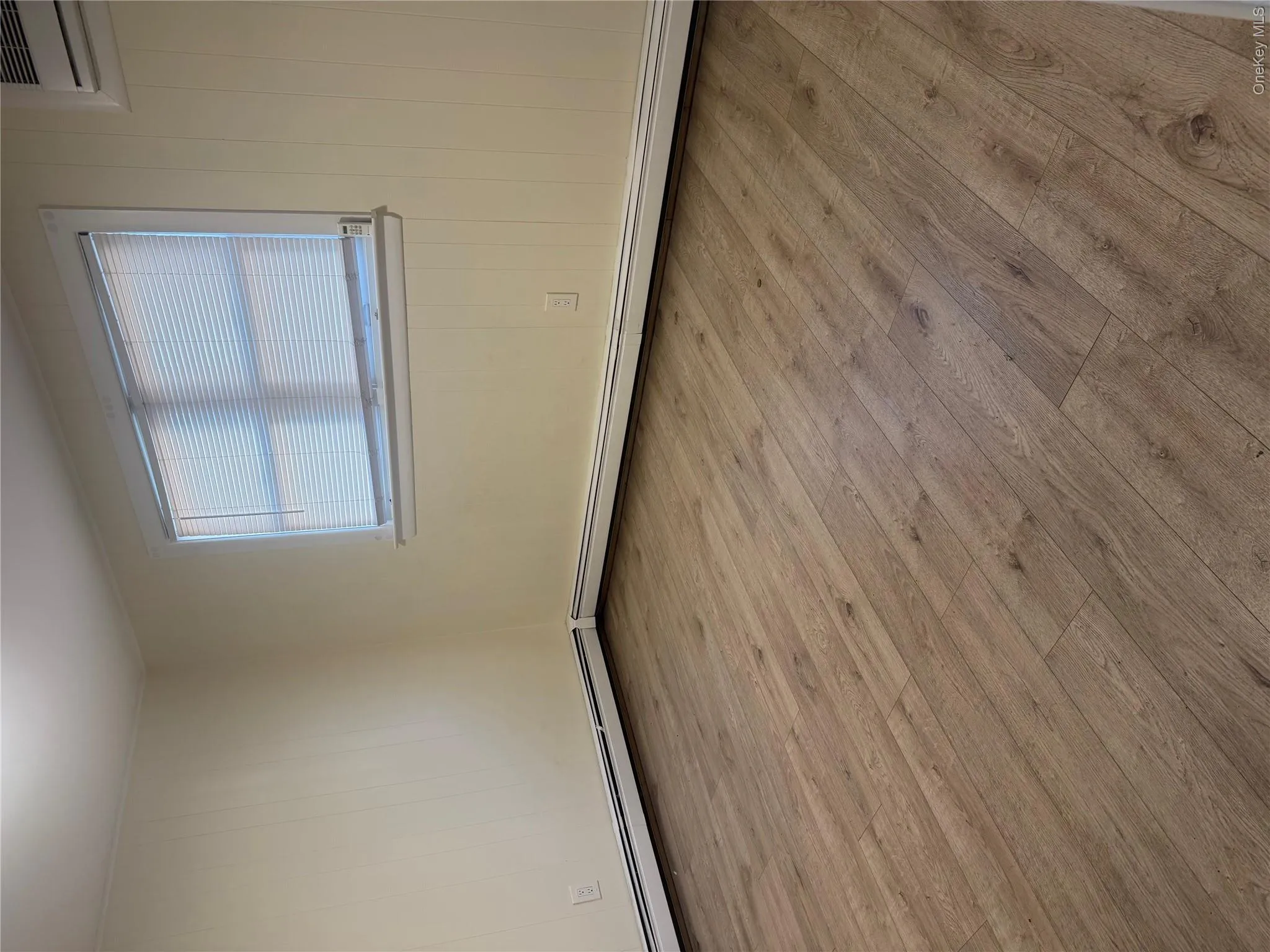 Wood-finish flooring with white trim and a single window featuring blinds Wood-finish flooring with white trim and a single window featuring blinds