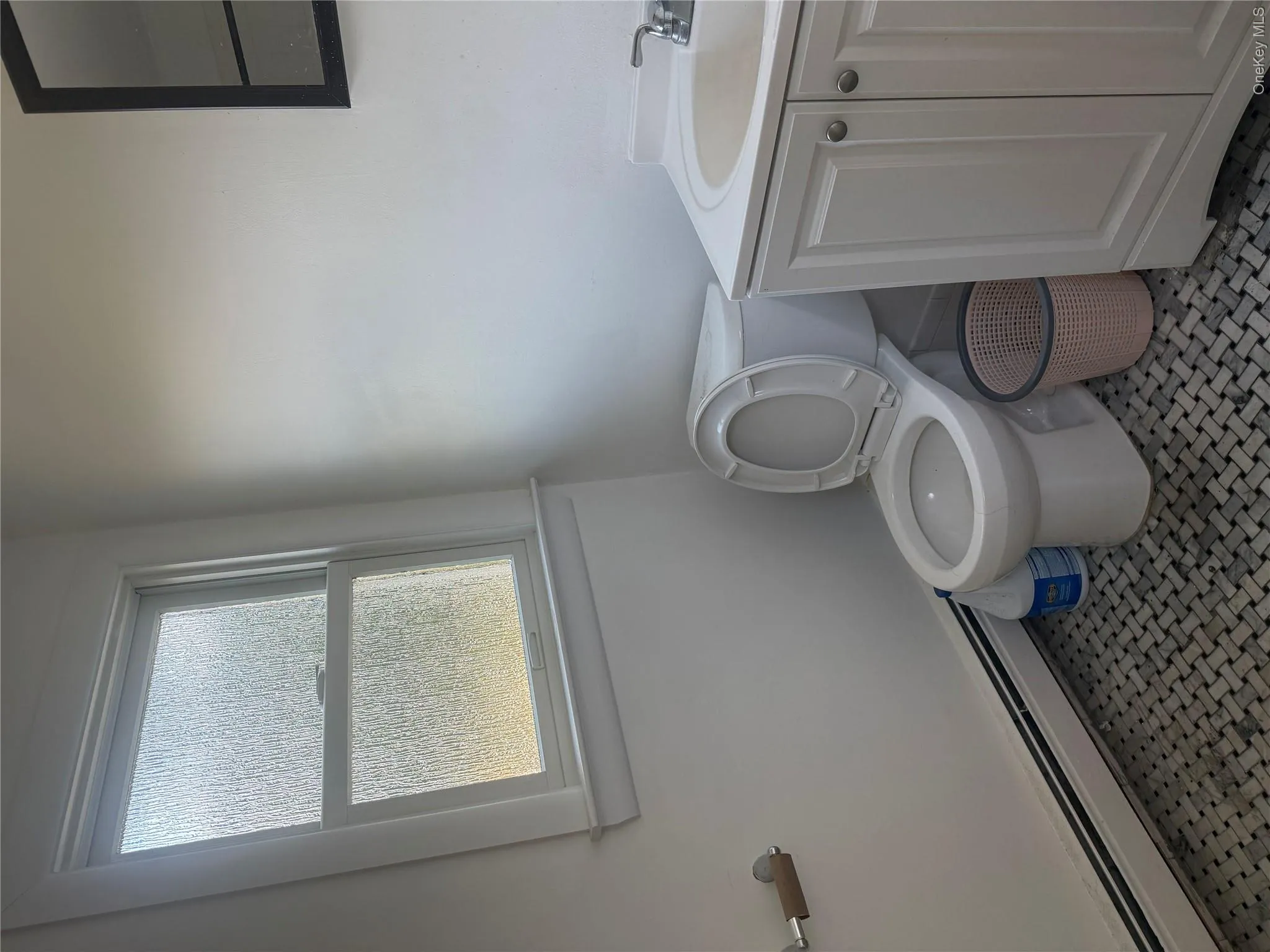 Frosted window, tiled flooring, built-in baseboard heating, white vanity with integrated sink, and a wall-mounted mirror Frosted window, tiled flooring, built-in baseboard heating, white vanity with integrated sink, and a wall-mounted mirror