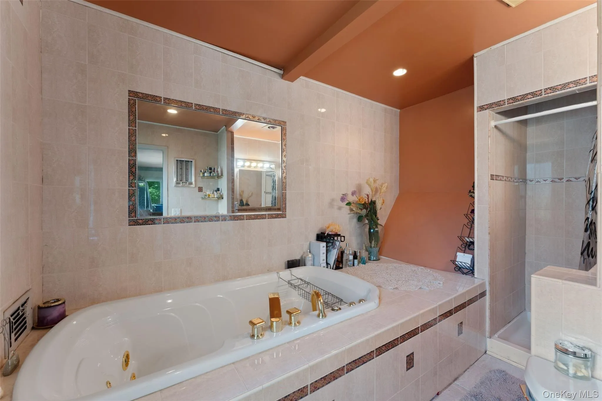 Tiled bathroom featuring a jacuzzi, built-in shower, vanity with sink, and wall-mounted lighting. Tiled bathroom featuring a jacuzzi, built-in shower, vanity with sink, and wall-mounted lighting.