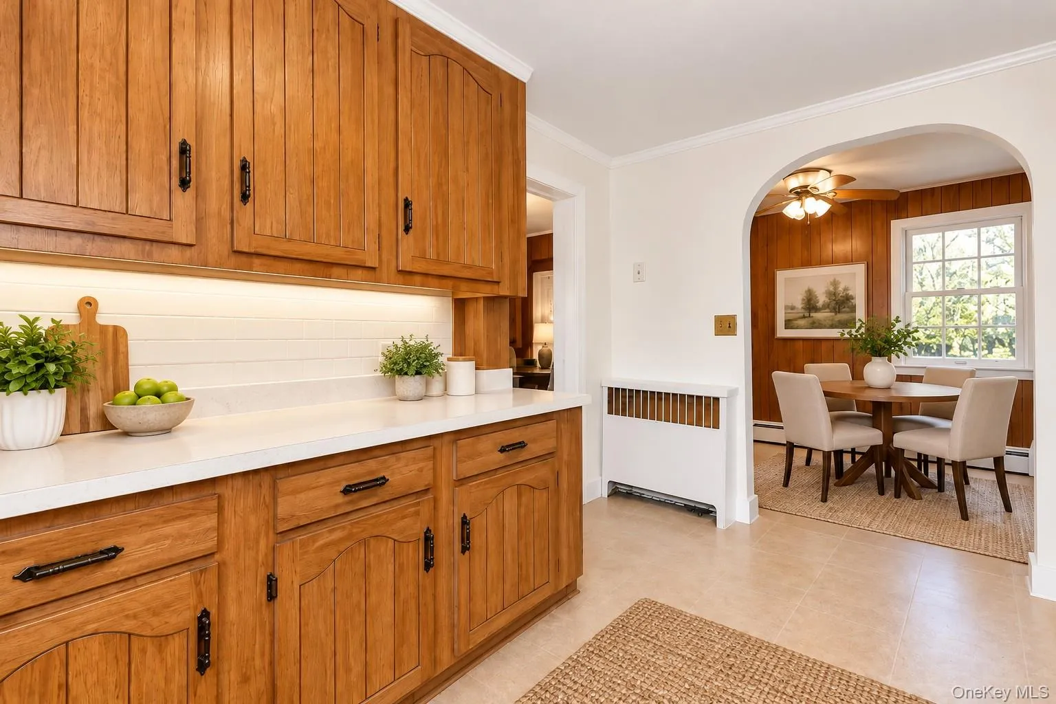 Virtually Staged Eat-In Kitchen and Dining AreaThis charming eat-in kitchen has been thoughtfully virtually staged to highlight its warmth, functionality, and inviting layout. Featuring beautiful natural wood cabinetry, generous countertop space, and ample storage, the kitchen blends classic character with everyday convenience. A graceful arched doorway leads to a cozy dining area accented by rich wood-paneled walls, a ceiling fan, and a large window that welcomes abundant natural light. Virtually furnished with a round dining table and comfortable seating, this delightful space is ideal for morning coffee, casual family meals, and intimate gatherings. The seamless connection between the kitchen and dining area creates a welcoming atmosphere for everyday living and entertaining. Virtually Staged Eat-In Kitchen and Dining AreaThis charming eat-in kitchen has been thoughtfully virtually staged to highlight its warmth, functionality, and inviting layout. Featuring beautiful natural wood cabinetry, generous countertop space, and ample storage, the kitchen blends classic character with everyday convenience. A graceful arched doorway leads to a cozy dining area accented by rich wood-paneled walls, a ceiling fan, and a large window that welcomes abundant natural light. Virtually furnished with a round dining table and comfortable seating, this delightful space is ideal for morning coffee, casual family meals, and intimate gatherings. The seamless connection between the kitchen and dining area creates a welcoming atmosphere for everyday living and entertaining.