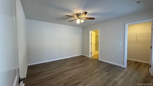 Unfurnished bedroom featuring ceiling fan, a spacious closet, dark wood-type flooring, and a closet Unfurnished bedroom featuring ceiling fan, a spacious closet, dark wood-type flooring, and a closet