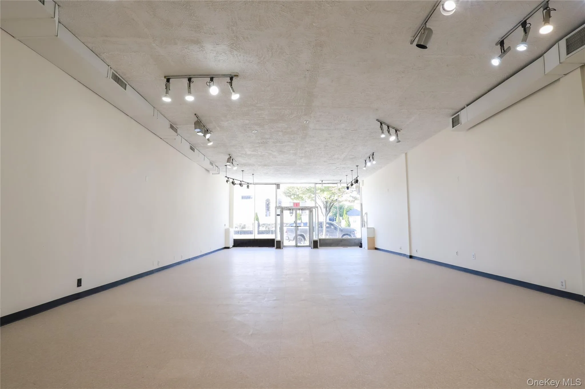 Expansive open-concept room with light-colored flooring, white walls, and track lighting fixtures Expansive open-concept room with light-colored flooring, white walls, and track lighting fixtures