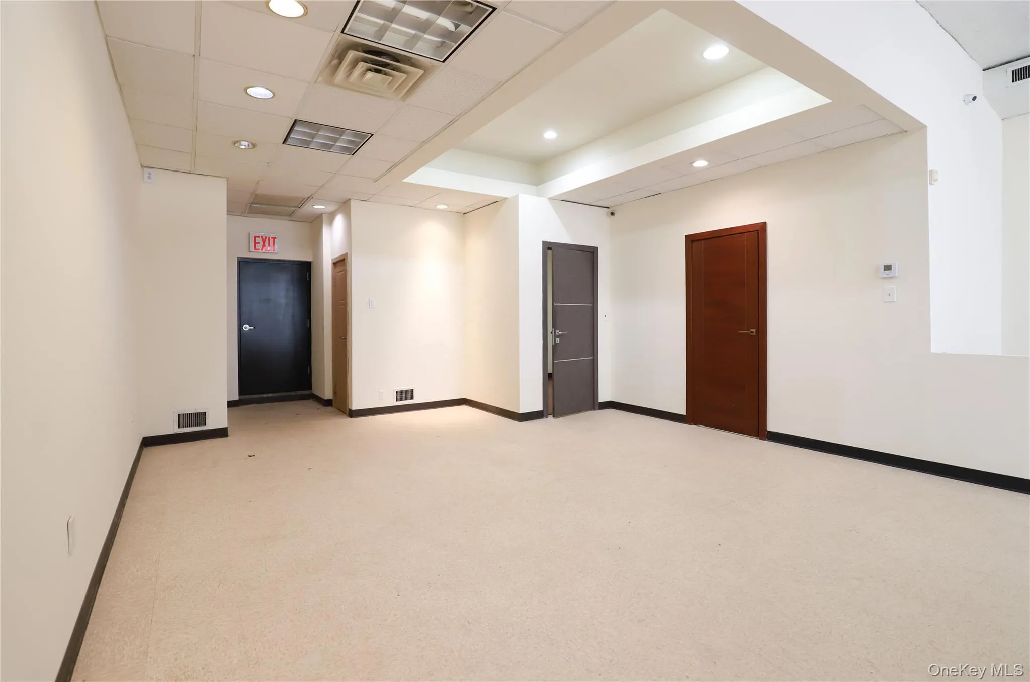 Recessed lighting, drop ceiling, light-colored carpeting, multiple doors, and a fire exit Recessed lighting, drop ceiling, light-colored carpeting, multiple doors, and a fire exit