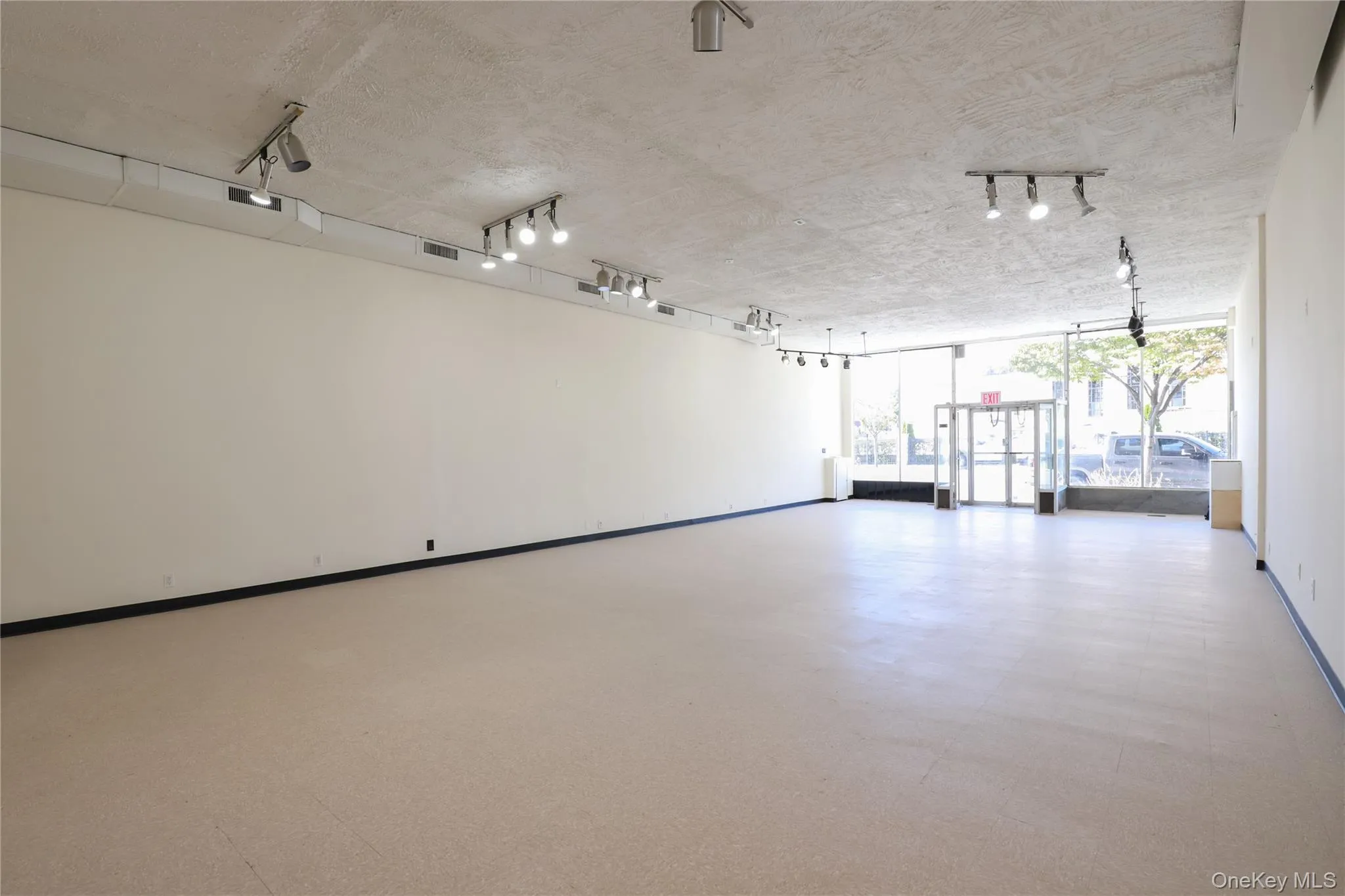 Expansive open-concept room with light-colored flooring, white walls, and track lighting fixtures Expansive open-concept room with light-colored flooring, white walls, and track lighting fixtures