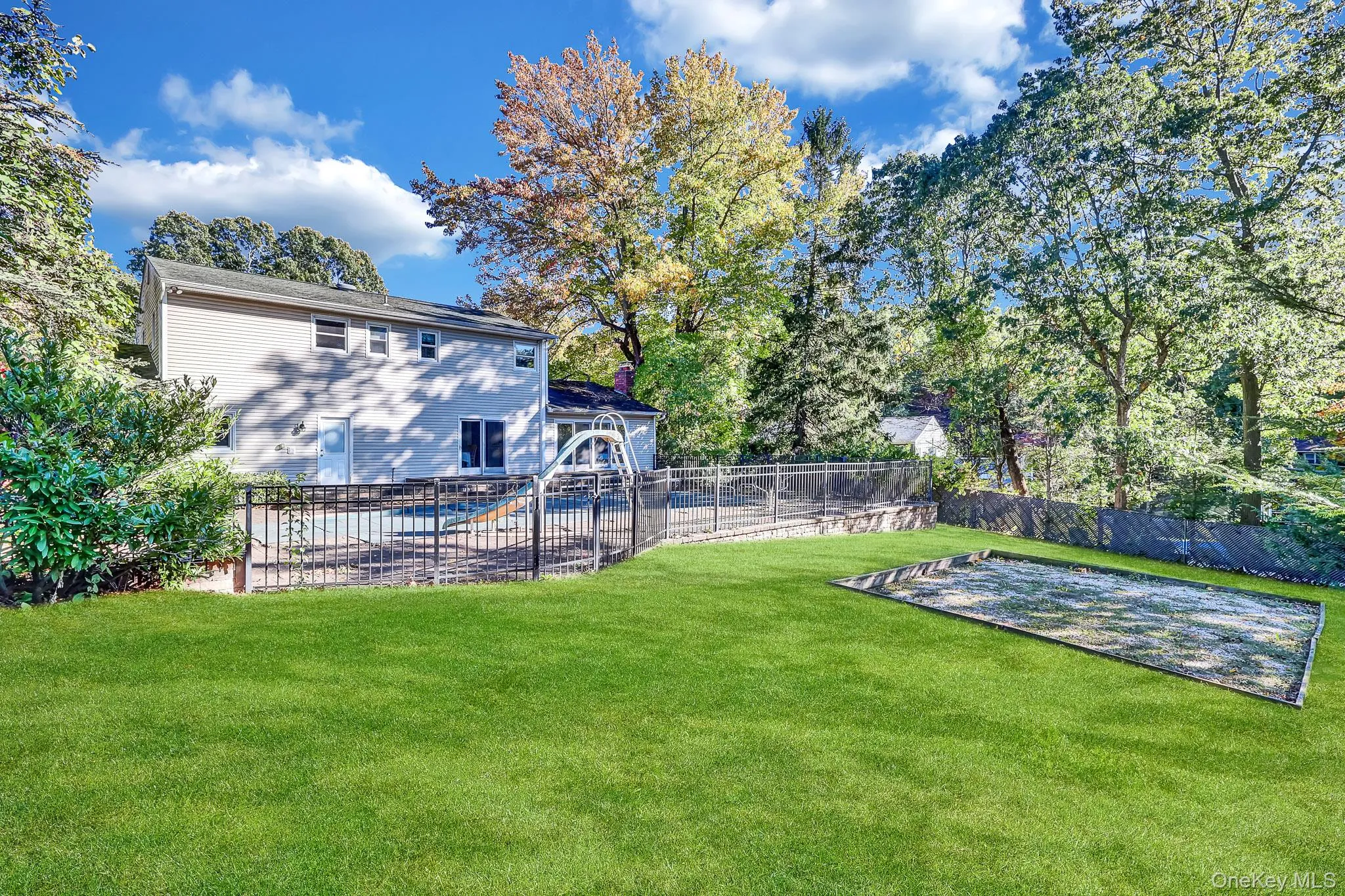 Backyard featuring a manicured lawn, fenced swimming pool with a slide, and a sand area Backyard featuring a manicured lawn, fenced swimming pool with a slide, and a sand area
