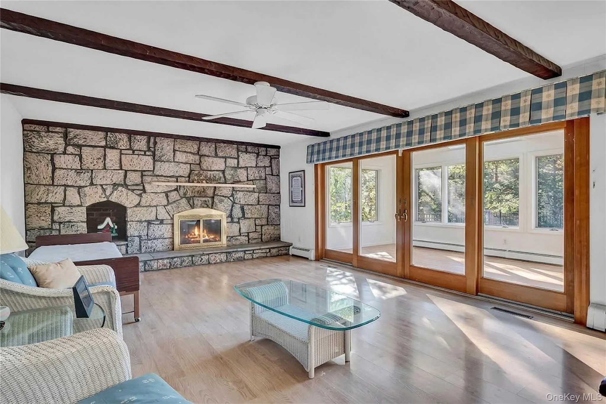 Living area featuring exposed wood ceiling beams, floor-to-ceiling stone fireplace with a raised hearth, wood-finish flooring, and multi-panel sliding glass doors with wood trim Living area featuring exposed wood ceiling beams, floor-to-ceiling stone fireplace with a raised hearth, wood-finish flooring, and multi-panel sliding glass doors with wood trim