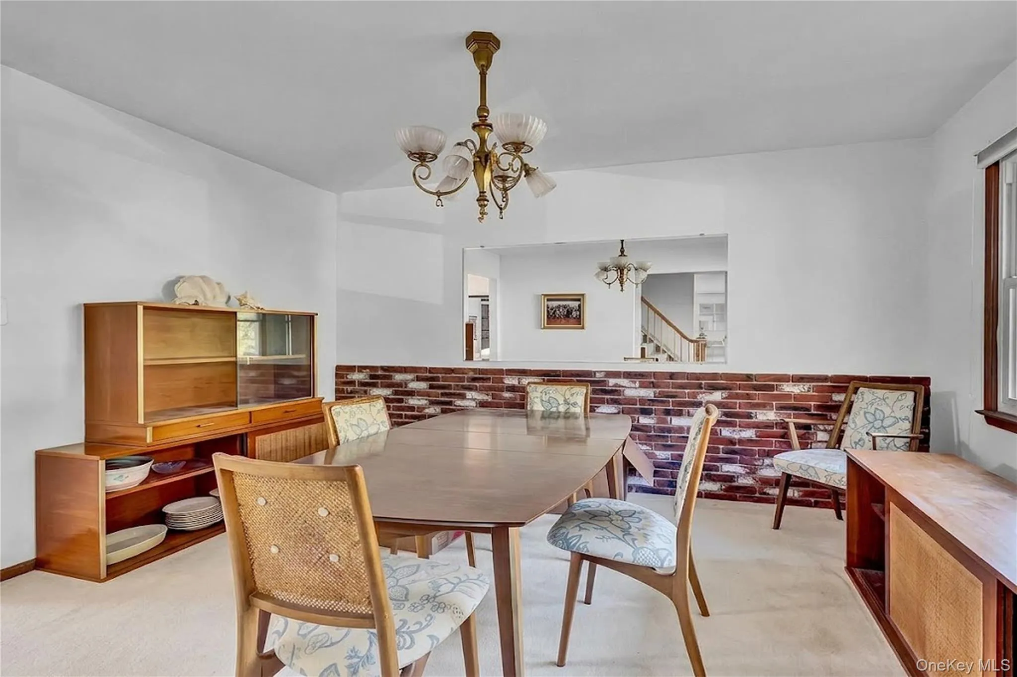 Dining area featuring an exposed brick accent wall, a large rectangular wall cutout, and a traditional multi-arm chandelier Dining area featuring an exposed brick accent wall, a large rectangular wall cutout, and a traditional multi-arm chandelier