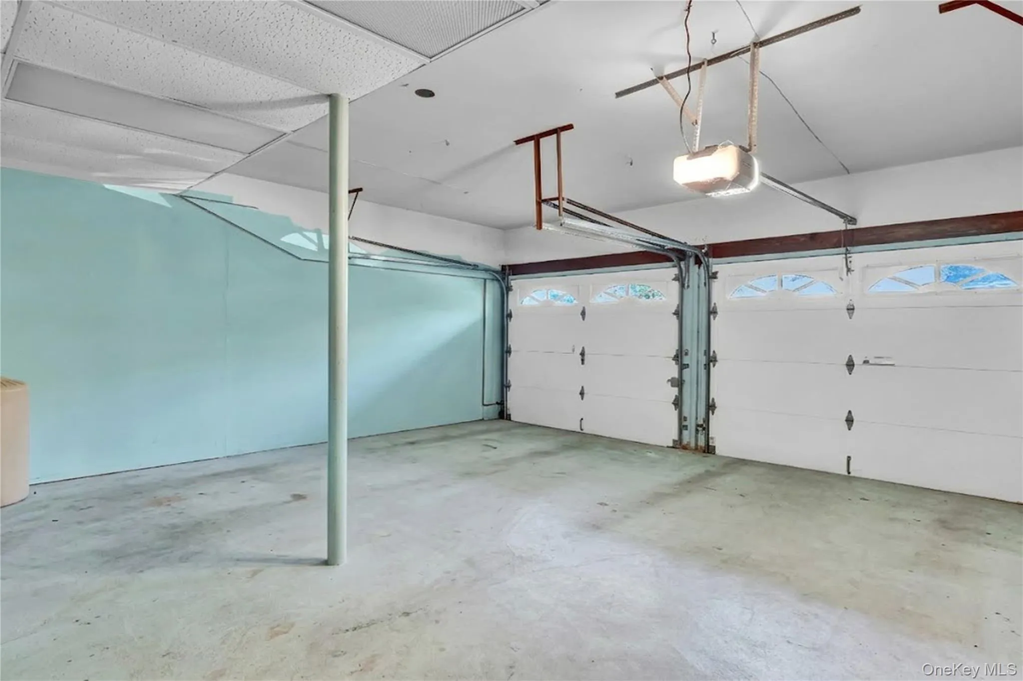 Attached two-car garage featuring dual overhead doors with glass panel inserts, concrete flooring, and ceiling-mounted automatic door openers Attached two-car garage featuring dual overhead doors with glass panel inserts, concrete flooring, and ceiling-mounted automatic door openers