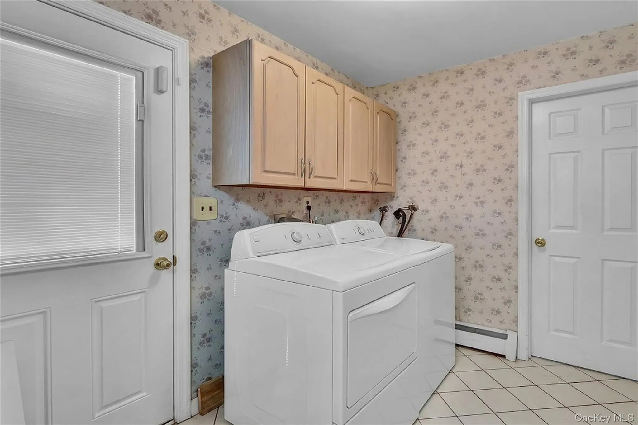 Utility space featuring light-toned wood-finish upper cabinetry, tiled flooring, and a six-panel door Utility space featuring light-toned wood-finish upper cabinetry, tiled flooring, and a six-panel door