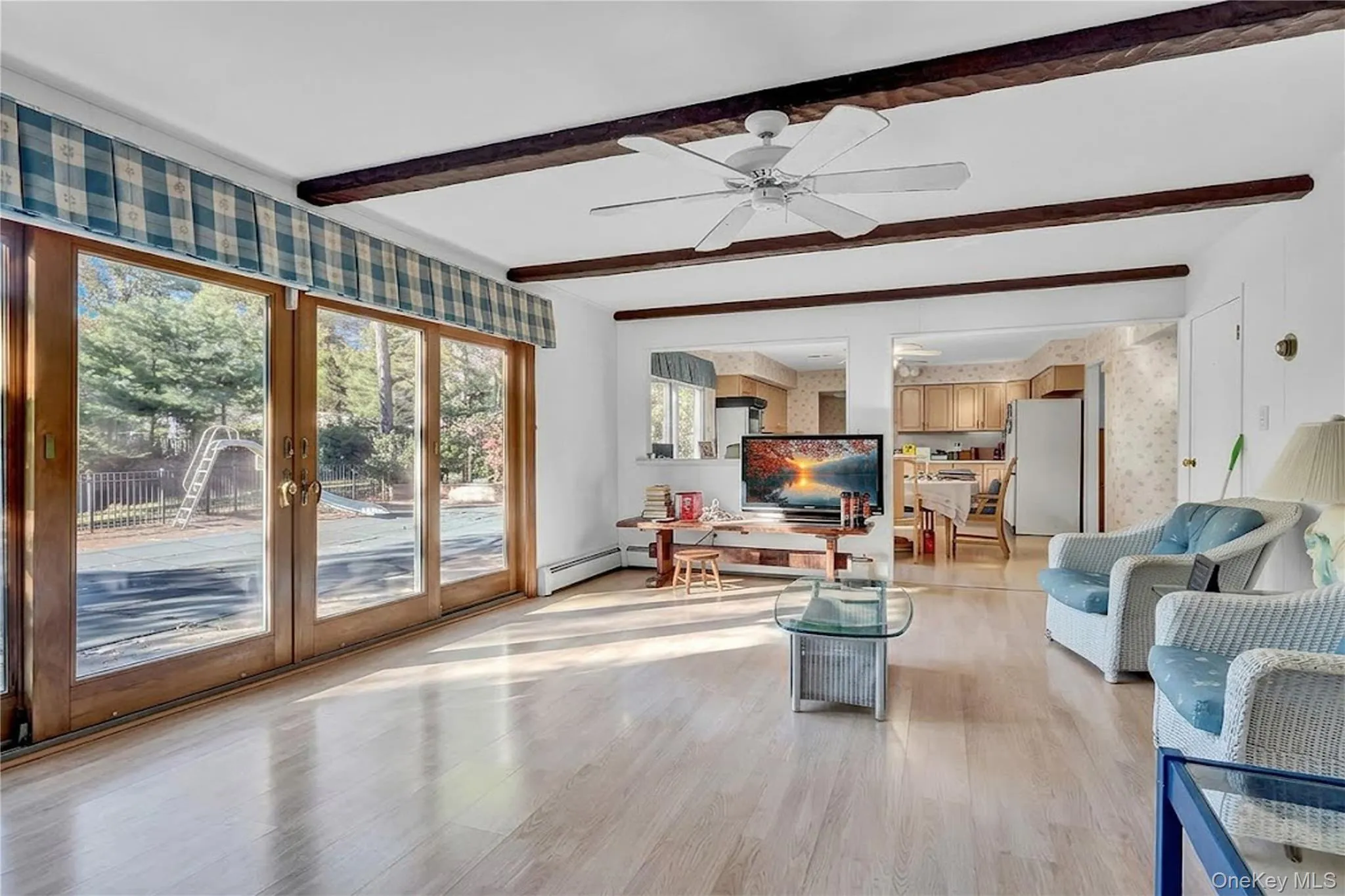 Living space featuring wood-finish flooring, exposed ceiling beams, a ceiling fan, and expansive glass sliding doors Living space featuring wood-finish flooring, exposed ceiling beams, a ceiling fan, and expansive glass sliding doors