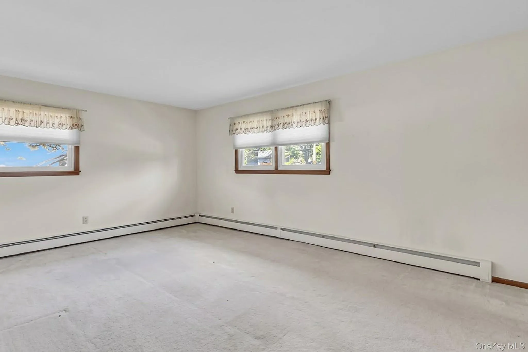 Neutral interior room featuring wall-to-wall carpeting and dual windows with wood-trimmed frames Neutral interior room featuring wall-to-wall carpeting and dual windows with wood-trimmed frames