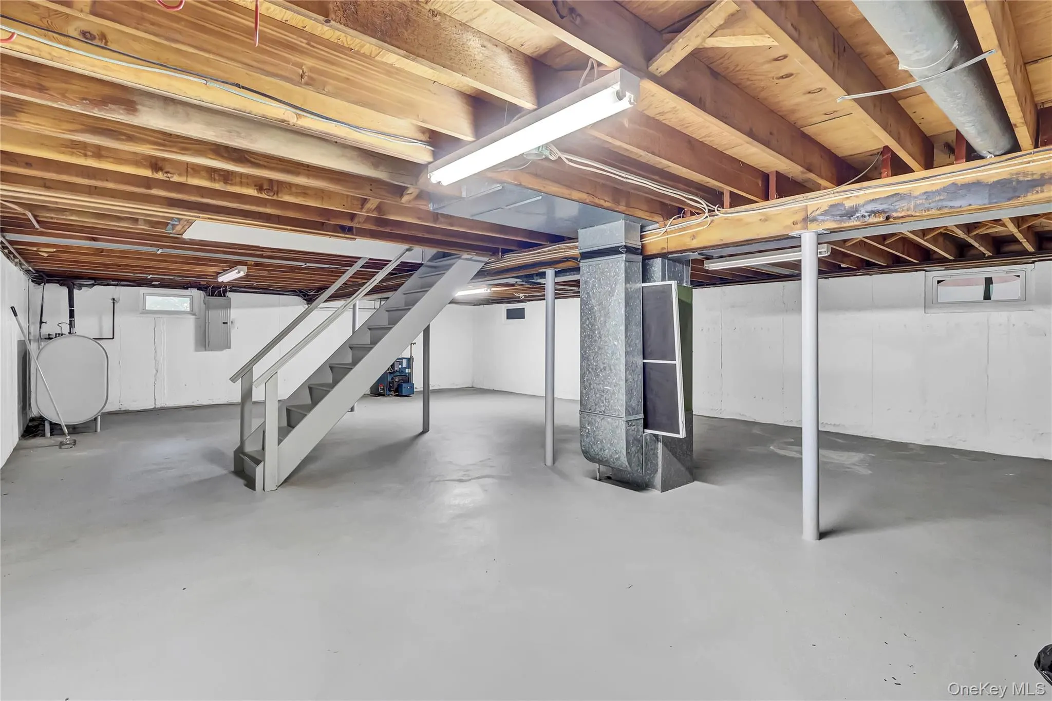 Unfinished lower level featuring exposed wood-beam ceiling construction, painted concrete flooring, structural steel support columns, and interior staircase with railing Unfinished lower level featuring exposed wood-beam ceiling construction, painted concrete flooring, structural steel support columns, and interior staircase with railing