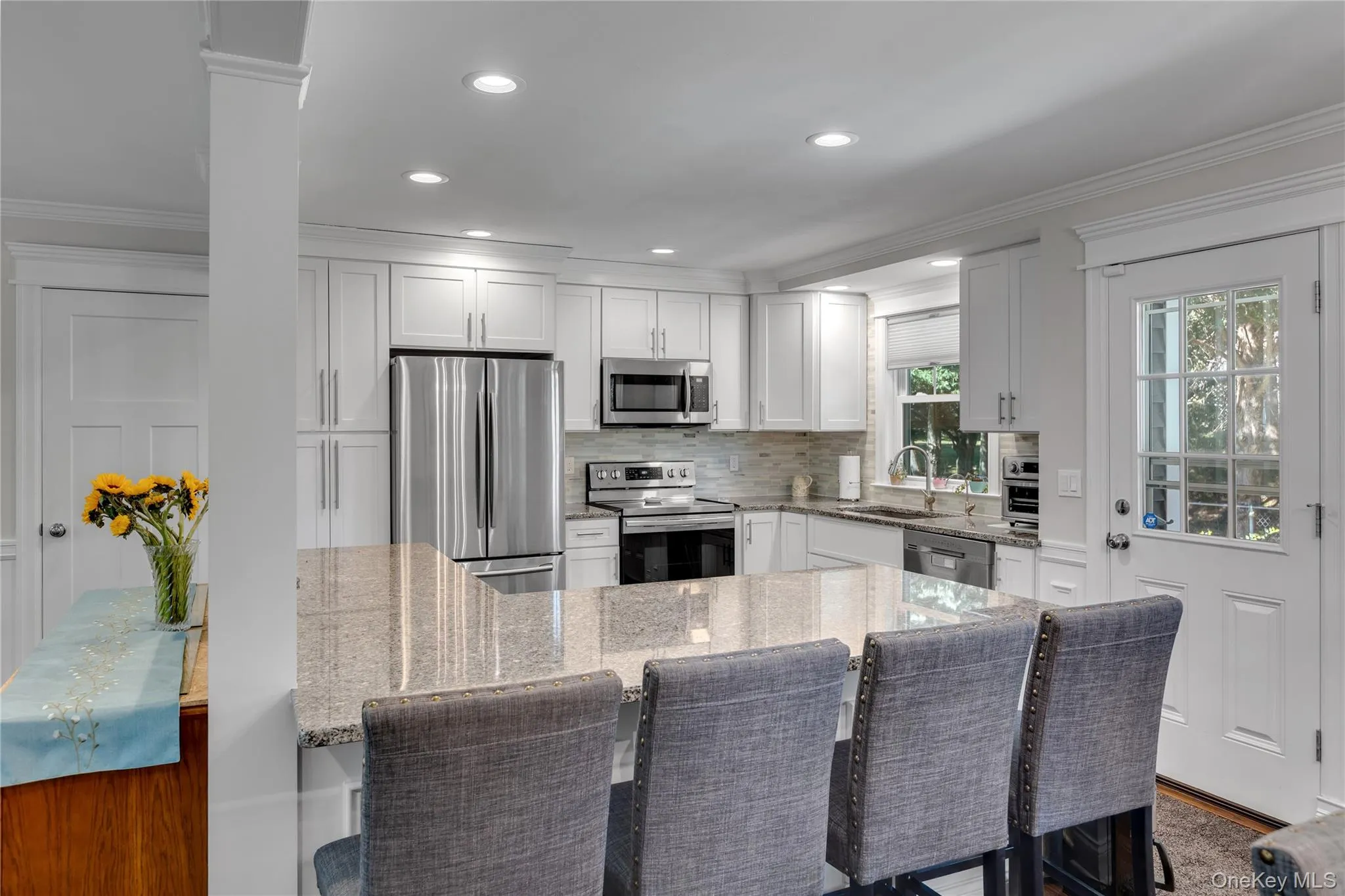 Kitchen featuring white cabinetry, stainless steel appliances, a large island with a stone countertop, and a glass-paned exterior door Kitchen featuring white cabinetry, stainless steel appliances, a large island with a stone countertop, and a glass-paned exterior door