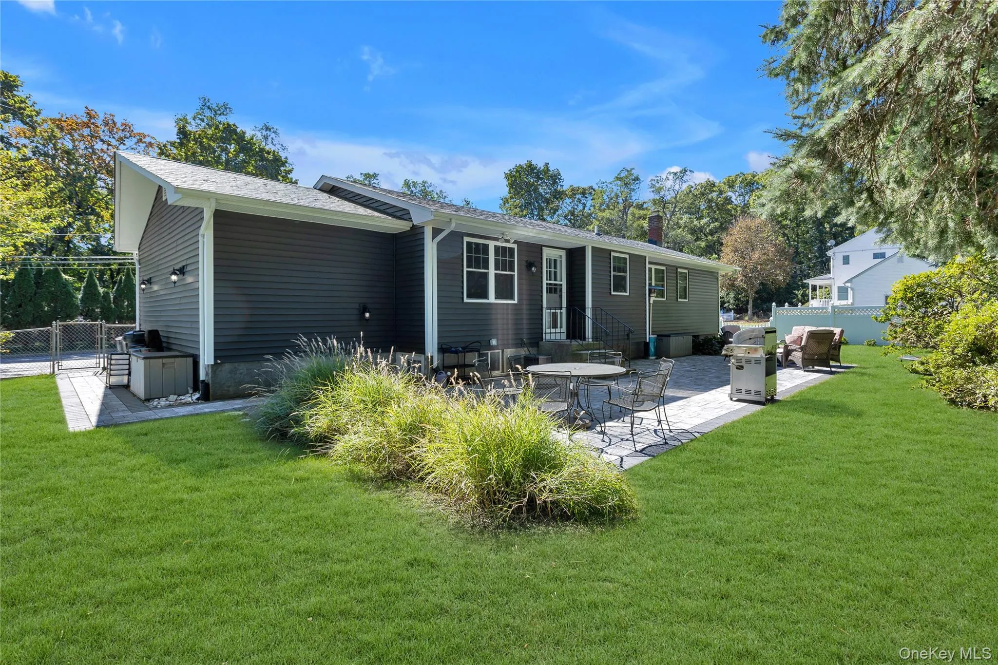 Expansive backyard featuring a manicured lawn, paver patio, mature trees, and dark gray siding Expansive backyard featuring a manicured lawn, paver patio, mature trees, and dark gray siding