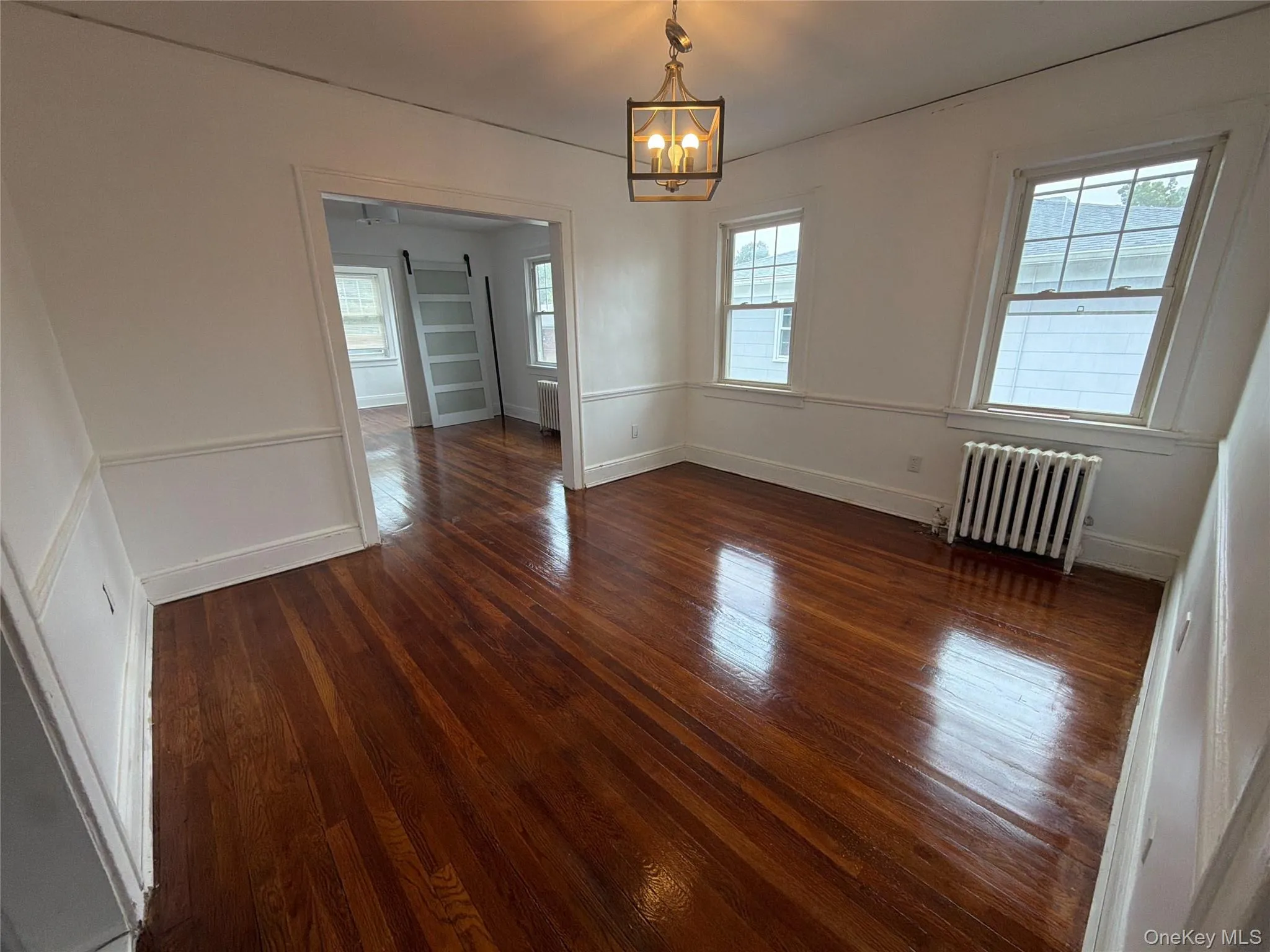 Living room Hardwood flooring throughout, white wainscoting, two windows, and an overhead light fixture Living room Hardwood flooring throughout, white wainscoting, two windows, and an overhead light fixture