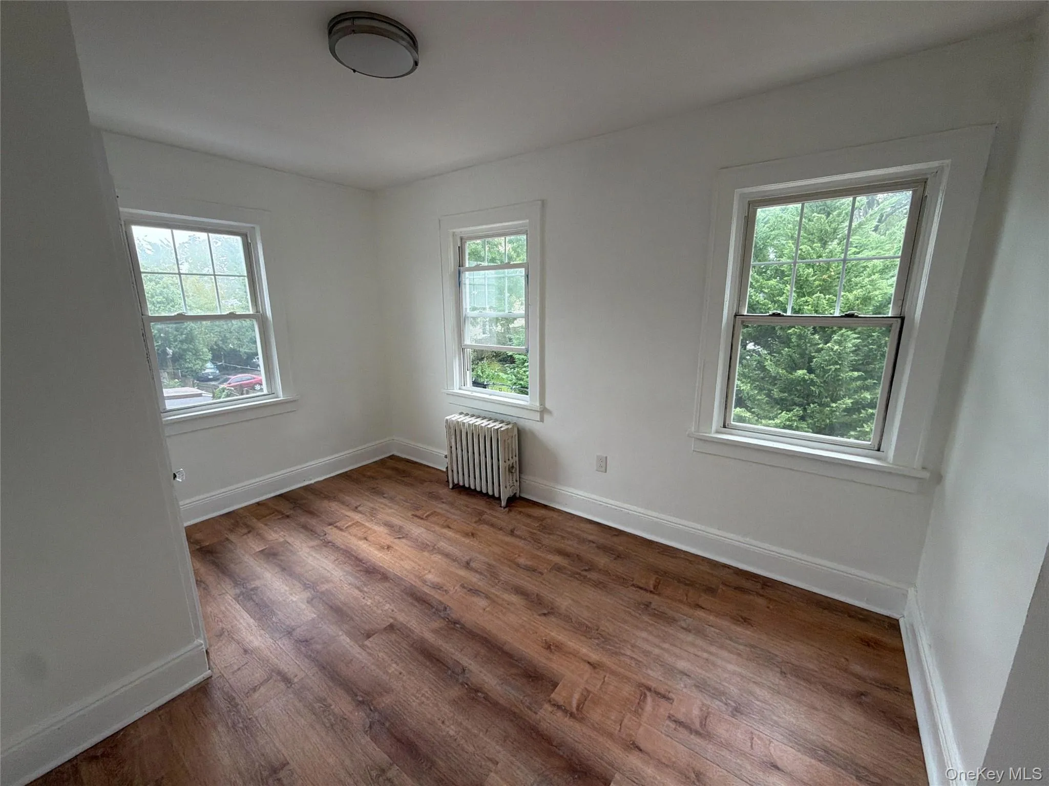 bedroom 1 Wood-finish flooring, white wall paint, two windows with white trim, and a flush mount ceiling light bedroom 1 Wood-finish flooring, white wall paint, two windows with white trim, and a flush mount ceiling light