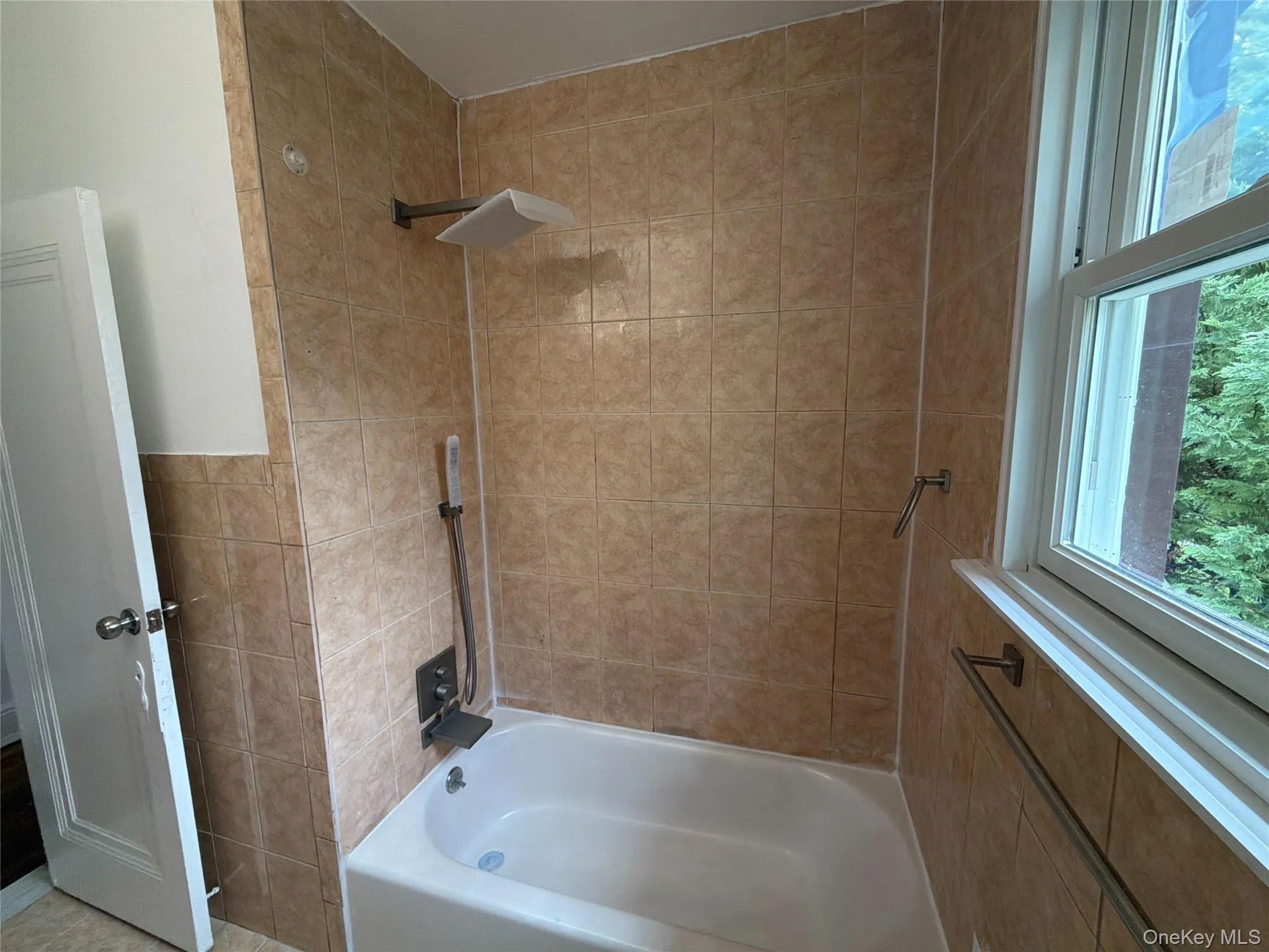 Bathtub with light-colored tile surround, featuring a rain shower head and a multi-function shower system Bathtub with light-colored tile surround, featuring a rain shower head and a multi-function shower system