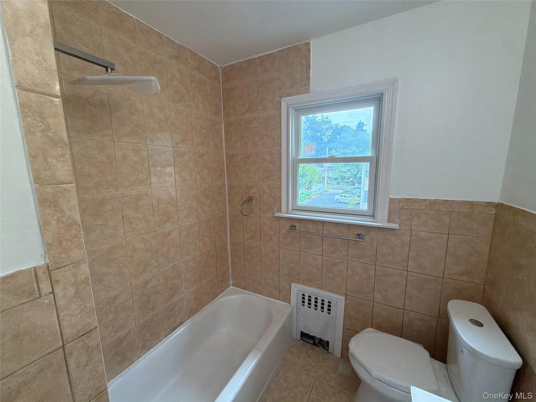 Enclosed shower and tub combination featuring tile surround, rain shower head, and an adjacent window with white trim Enclosed shower and tub combination featuring tile surround, rain shower head, and an adjacent window with white trim