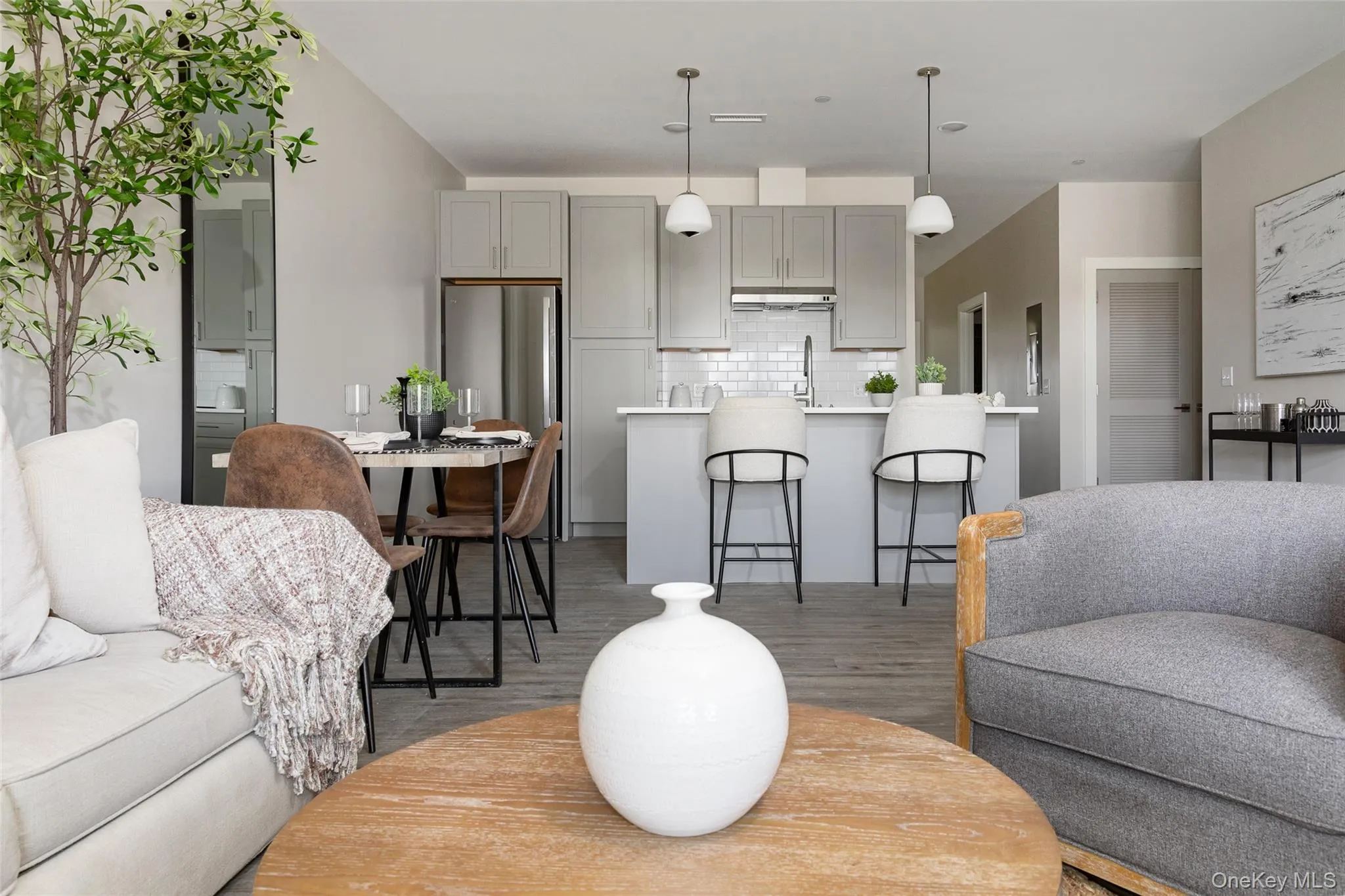 Open-concept living area with wood-finish flooring, white subway tile backsplash, stainless steel appliances, and pendant lighting Open-concept living area with wood-finish flooring, white subway tile backsplash, stainless steel appliances, and pendant lighting