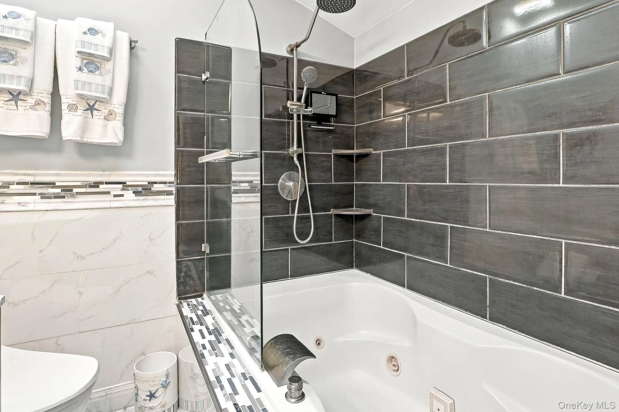Bathtub with a glass shower panel, dark subway tile surround, integrated shelving, and a rain showerhead Bathtub with a glass shower panel, dark subway tile surround, integrated shelving, and a rain showerhead