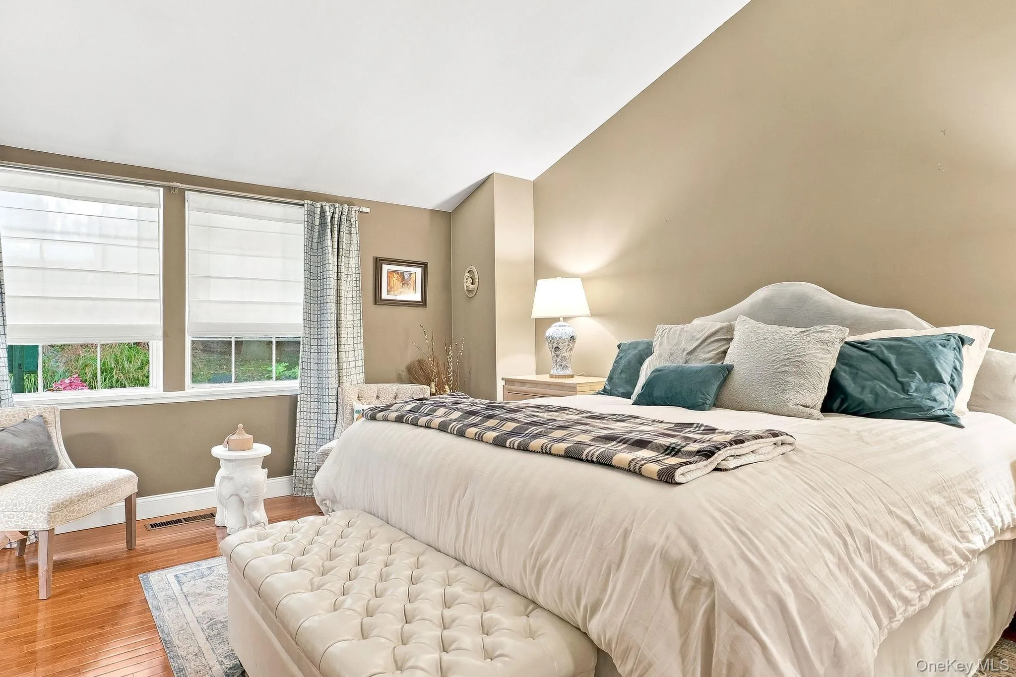 Hardwood flooring, two windows with Roman shades, upholstered headboard, pitched ceiling, and neutral wall tones Hardwood flooring, two windows with Roman shades, upholstered headboard, pitched ceiling, and neutral wall tones