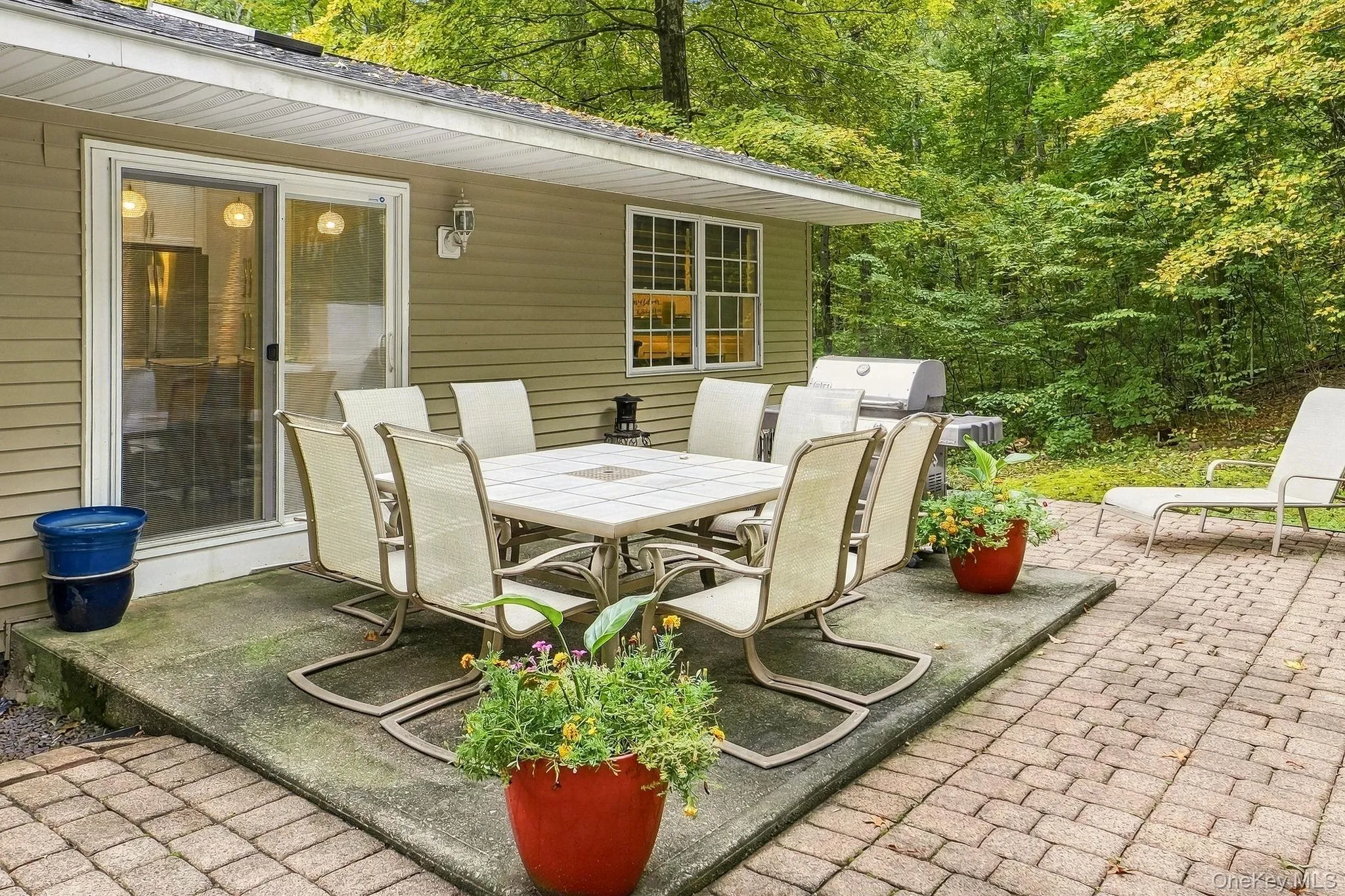 Patio area featuring a sliding glass door, a brick paver section, and mature trees in the background Patio area featuring a sliding glass door, a brick paver section, and mature trees in the background