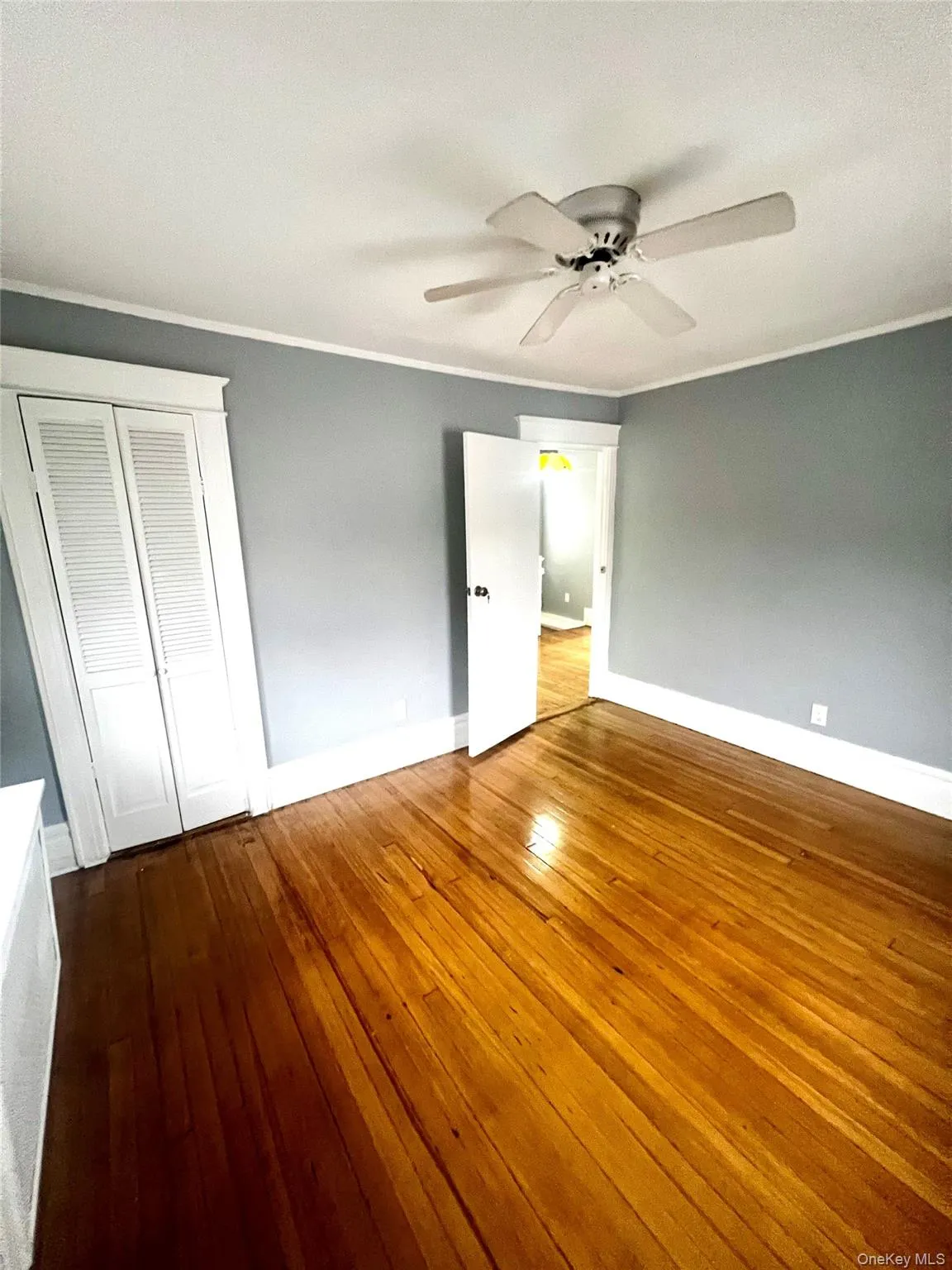 Unfurnished bedroom featuring ornamental molding, dark wood-style flooring, a closet, and ceiling fan Unfurnished bedroom featuring ornamental molding, dark wood-style flooring, a closet, and ceiling fan