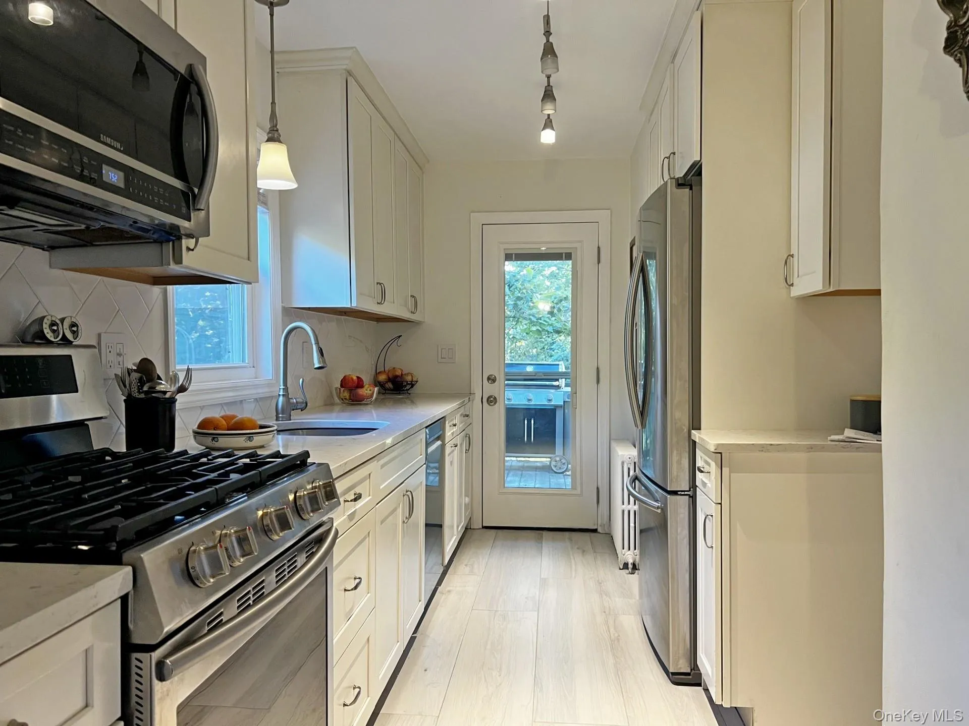 Kitchen with appliances with stainless steel finishes, pendant lighting, light stone counters, white cabinets, and light wood-style floors Kitchen with appliances with stainless steel finishes, pendant lighting, light stone counters, white cabinets, and light wood-style floors