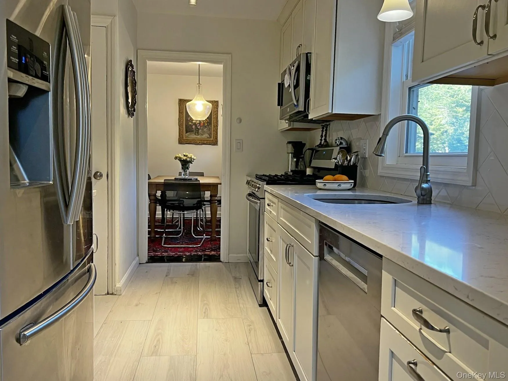 Kitchen featuring appliances with stainless steel finishes, decorative light fixtures, white cabinets, and light stone countertops Kitchen featuring appliances with stainless steel finishes, decorative light fixtures, white cabinets, and light stone countertops
