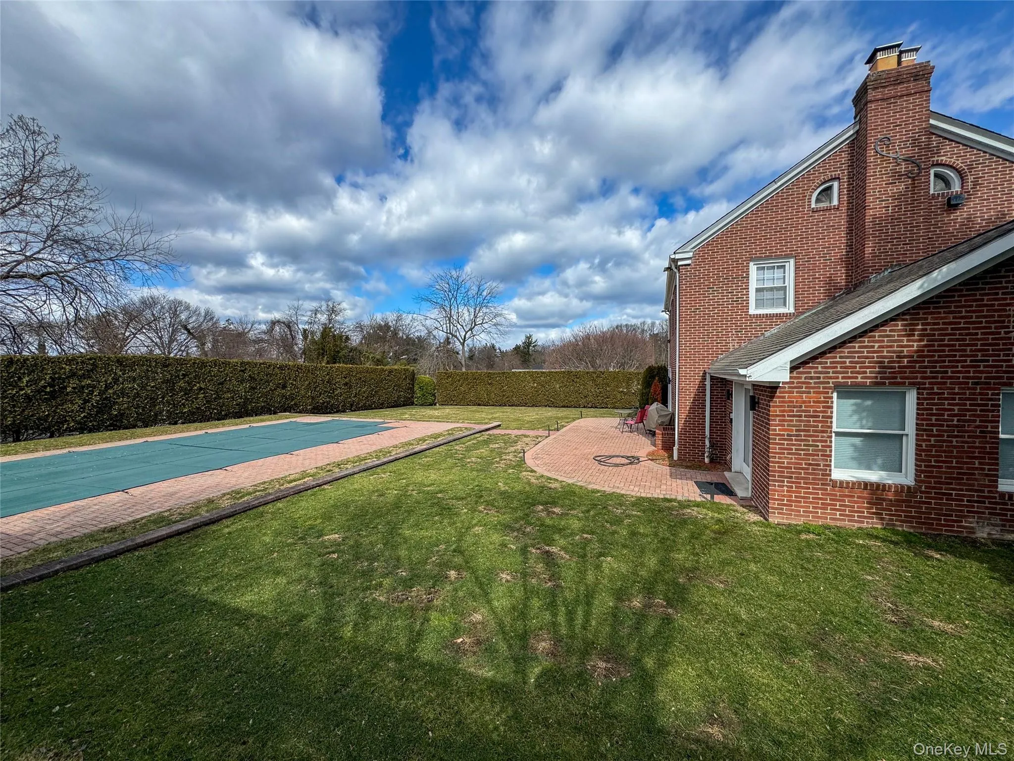 Brick exterior with a prominent chimney, a covered pool area, a paver patio, and mature perimeter hedging Brick exterior with a prominent chimney, a covered pool area, a paver patio, and mature perimeter hedging