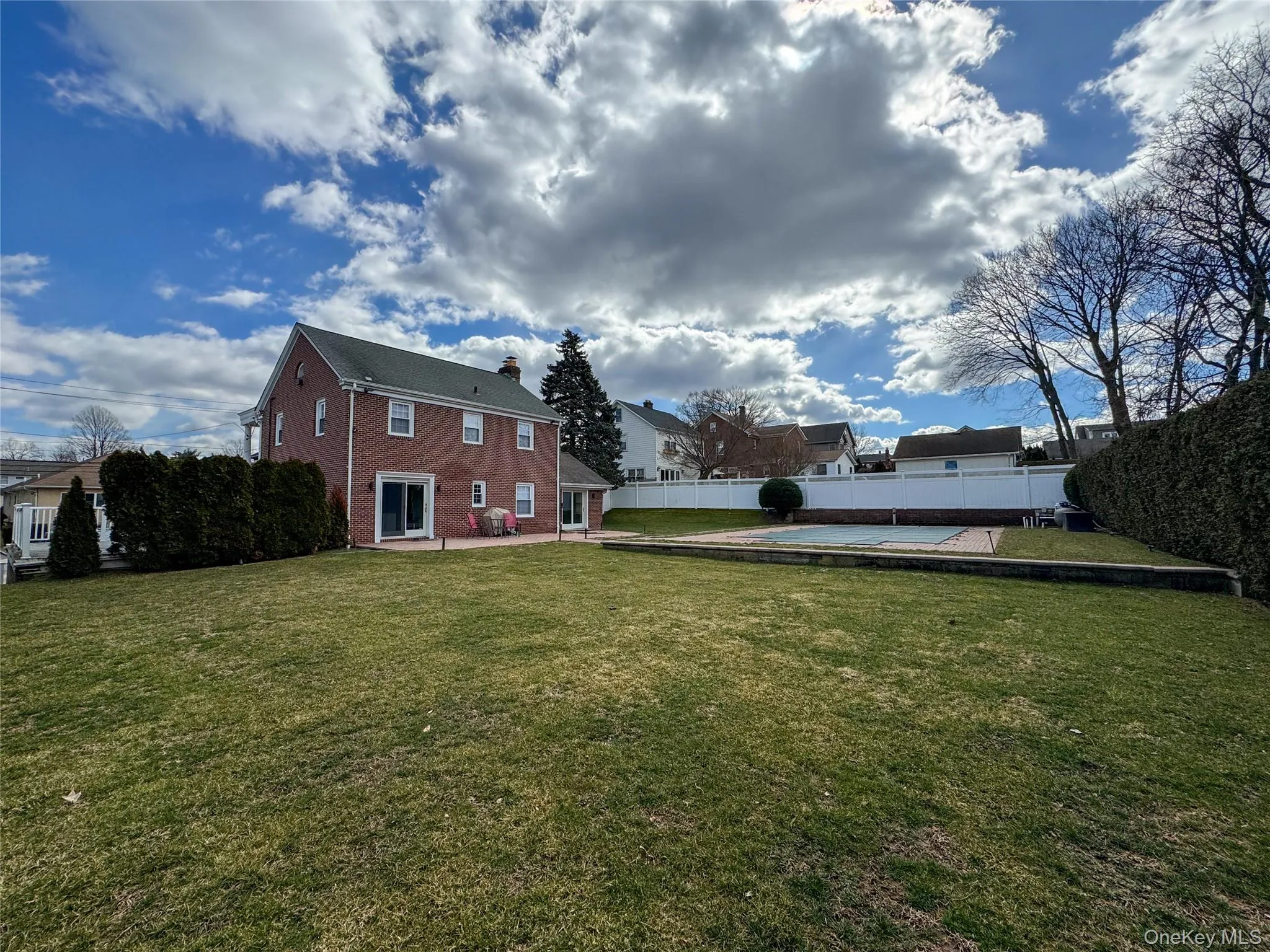 Brick exterior with multiple windows, multiple sliding glass doors, a patio, a lush lawn, and an in-ground pool Brick exterior with multiple windows, multiple sliding glass doors, a patio, a lush lawn, and an in-ground pool