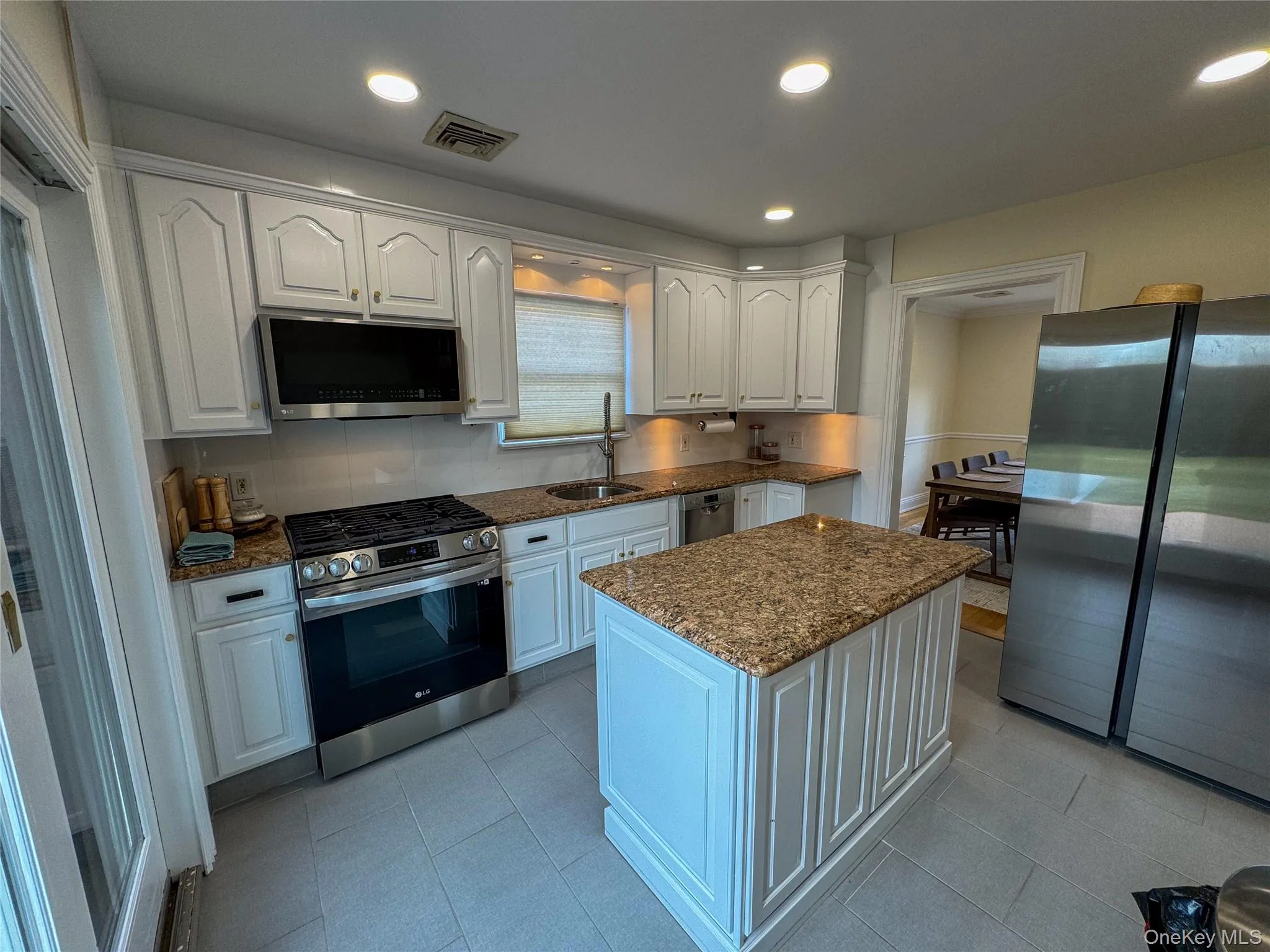 Kitchen featuring white cabinetry, granite countertops, stainless steel appliances, a center island, and tile flooring Kitchen featuring white cabinetry, granite countertops, stainless steel appliances, a center island, and tile flooring