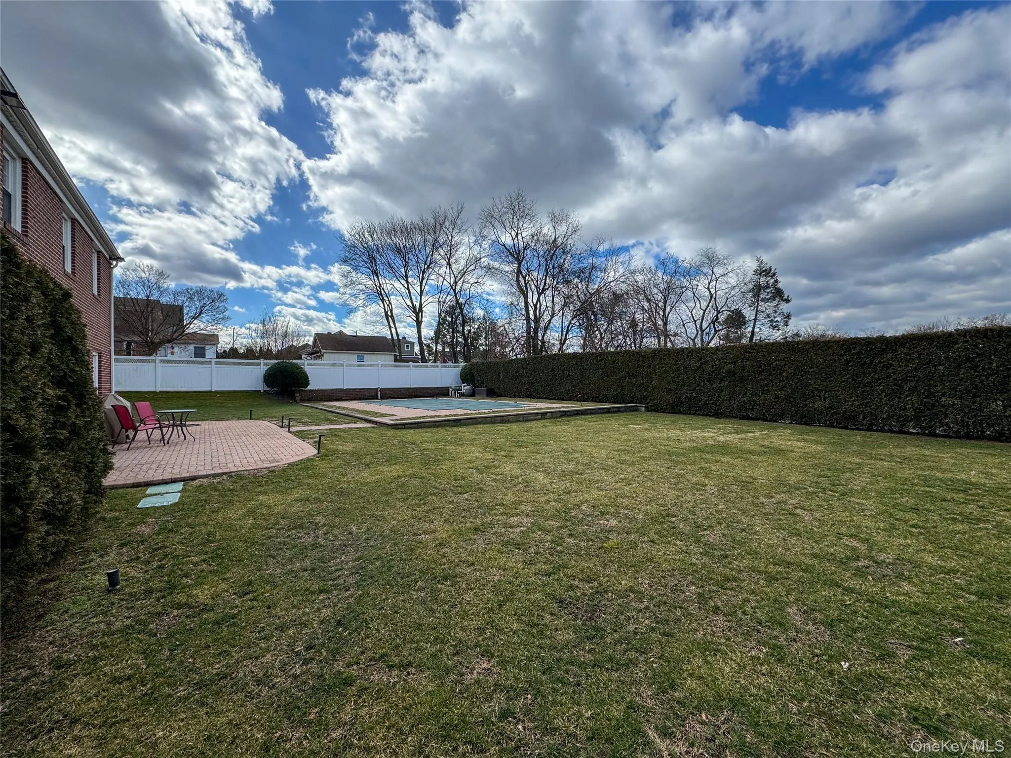 Expansive green lawn with a brick paver patio, mature privacy hedges, and a covered swimming pool Expansive green lawn with a brick paver patio, mature privacy hedges, and a covered swimming pool