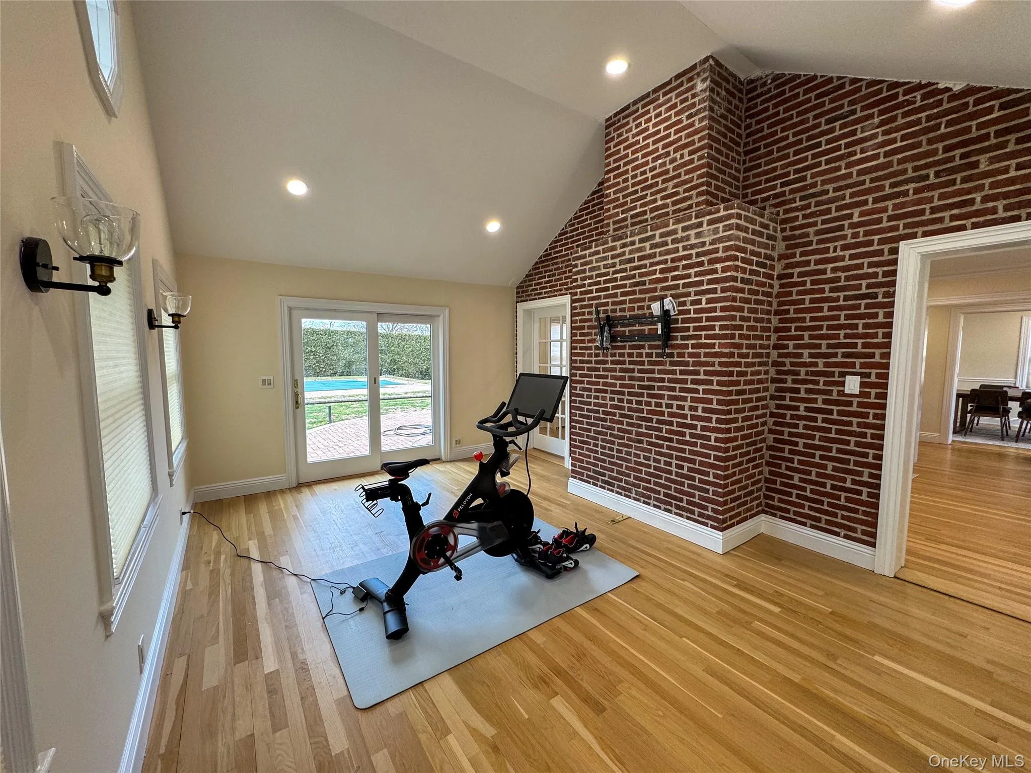 Vaulted ceiling with recessed lighting, exposed brick wall, light wood-finish flooring, sliding glass doors, and wall sconces Vaulted ceiling with recessed lighting, exposed brick wall, light wood-finish flooring, sliding glass doors, and wall sconces