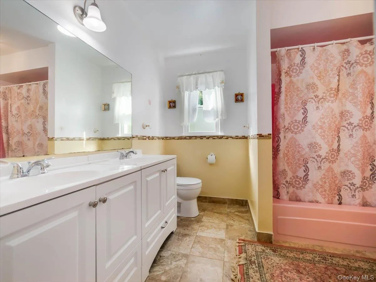 Dual-sink vanity with white cabinetry, oversized wall-mounted mirror, mosaic tile backsplash, and stone-finish flooring Dual-sink vanity with white cabinetry, oversized wall-mounted mirror, mosaic tile backsplash, and stone-finish flooring