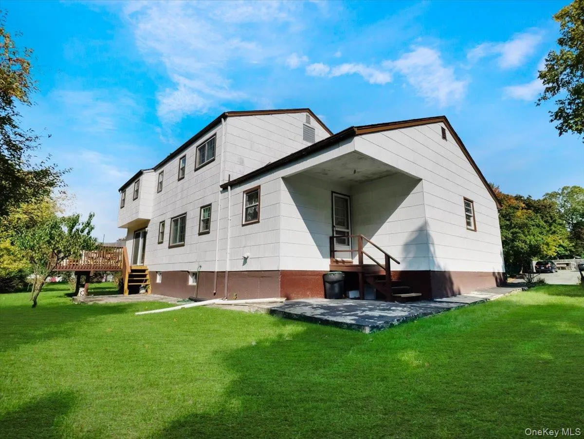 Exterior featuring a two-story structure with a concrete patio, elevated wooden deck, stairs, and a level lawn Exterior featuring a two-story structure with a concrete patio, elevated wooden deck, stairs, and a level lawn