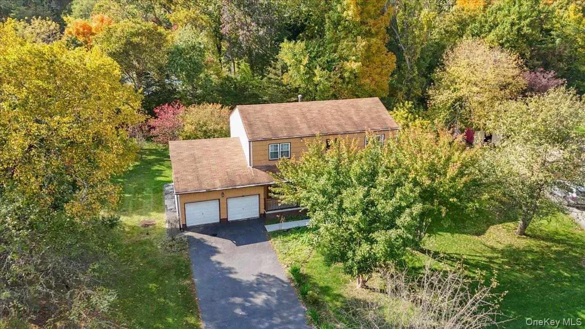 Two-story residence featuring light-toned exterior siding, a shingled roof, an attached two-car garage, and an asphalt driveway, all situated on a lot with mature tree coverage Two-story residence featuring light-toned exterior siding, a shingled roof, an attached two-car garage, and an asphalt driveway, all situated on a lot with mature tree coverage
