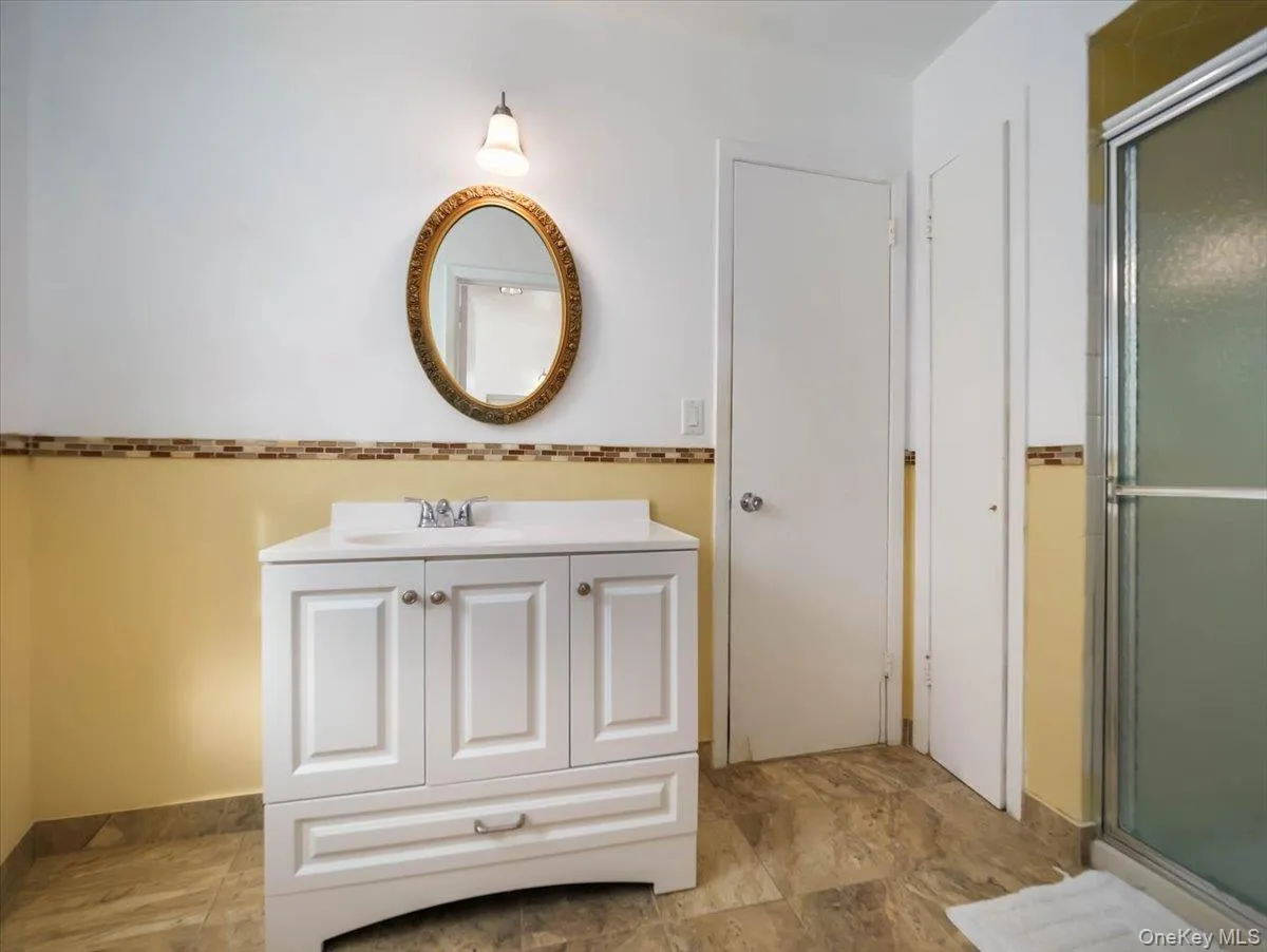 White vanity with integrated sink, stone-finish tile flooring, walk-in shower enclosure, and decorative tile backsplash White vanity with integrated sink, stone-finish tile flooring, walk-in shower enclosure, and decorative tile backsplash