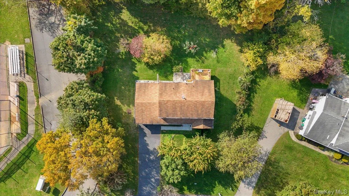 Aerial view of a residential lot featuring a shingled roof, paved driveway, expansive lawn, and mature trees Aerial view of a residential lot featuring a shingled roof, paved driveway, expansive lawn, and mature trees