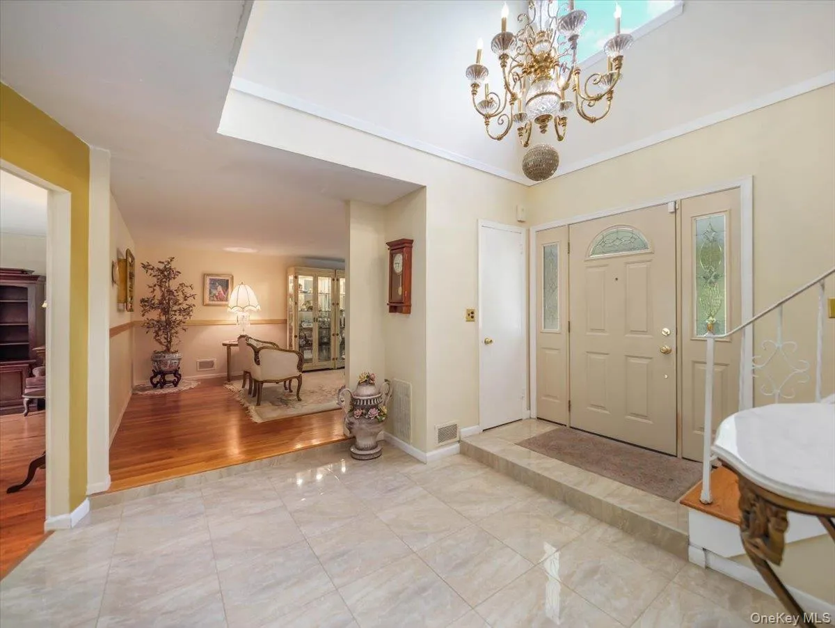 Entryway featuring large-format tile flooring, a recessed ceiling with a decorative chandelier, and a front door with glass sidelights and transom window Entryway featuring large-format tile flooring, a recessed ceiling with a decorative chandelier, and a front door with glass sidelights and transom window