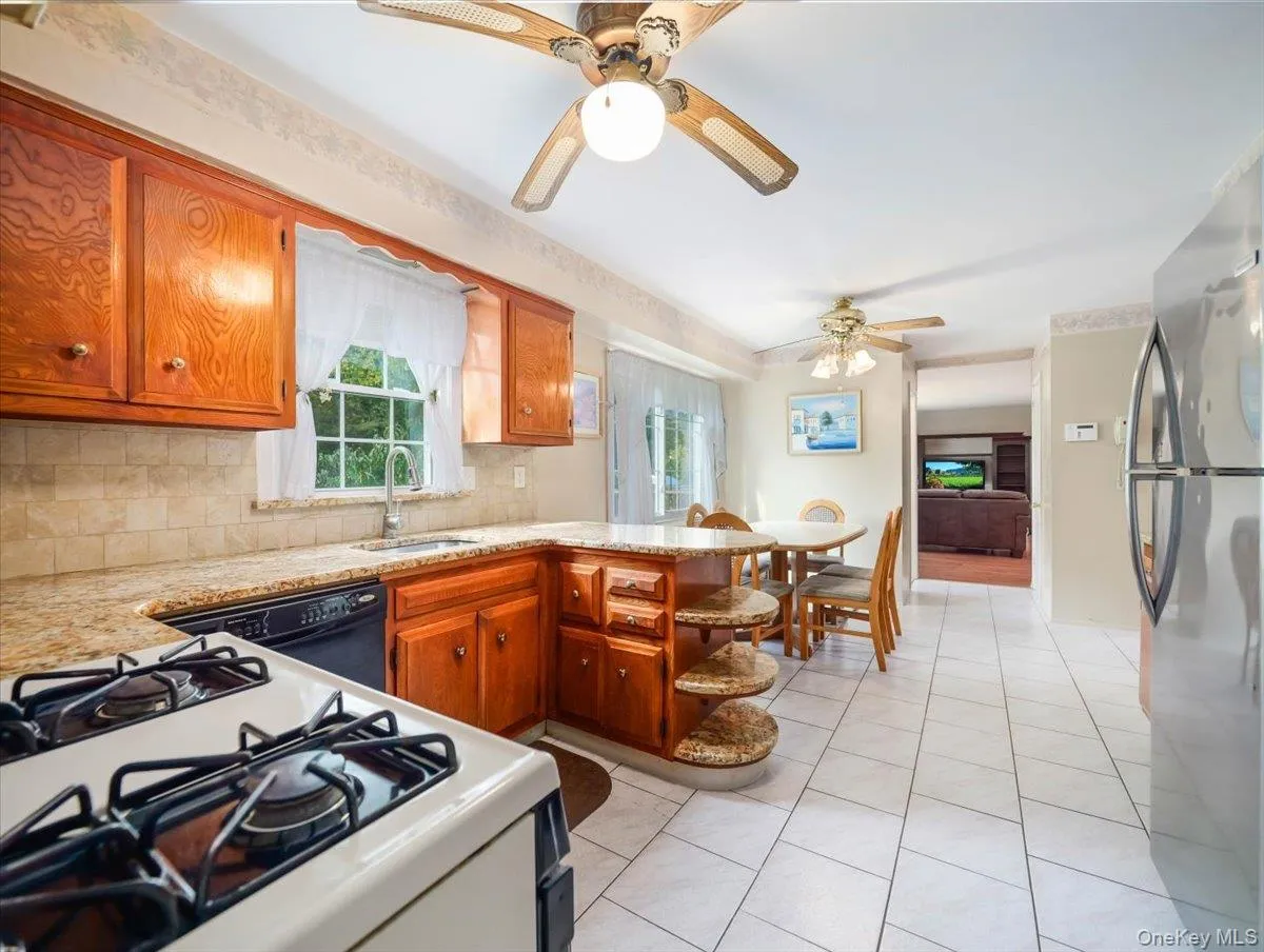 Kitchen featuring natural-finish wood cabinetry, stone-surface countertops, tile backsplash, tile flooring, and stainless steel appliances Kitchen featuring natural-finish wood cabinetry, stone-surface countertops, tile backsplash, tile flooring, and stainless steel appliances